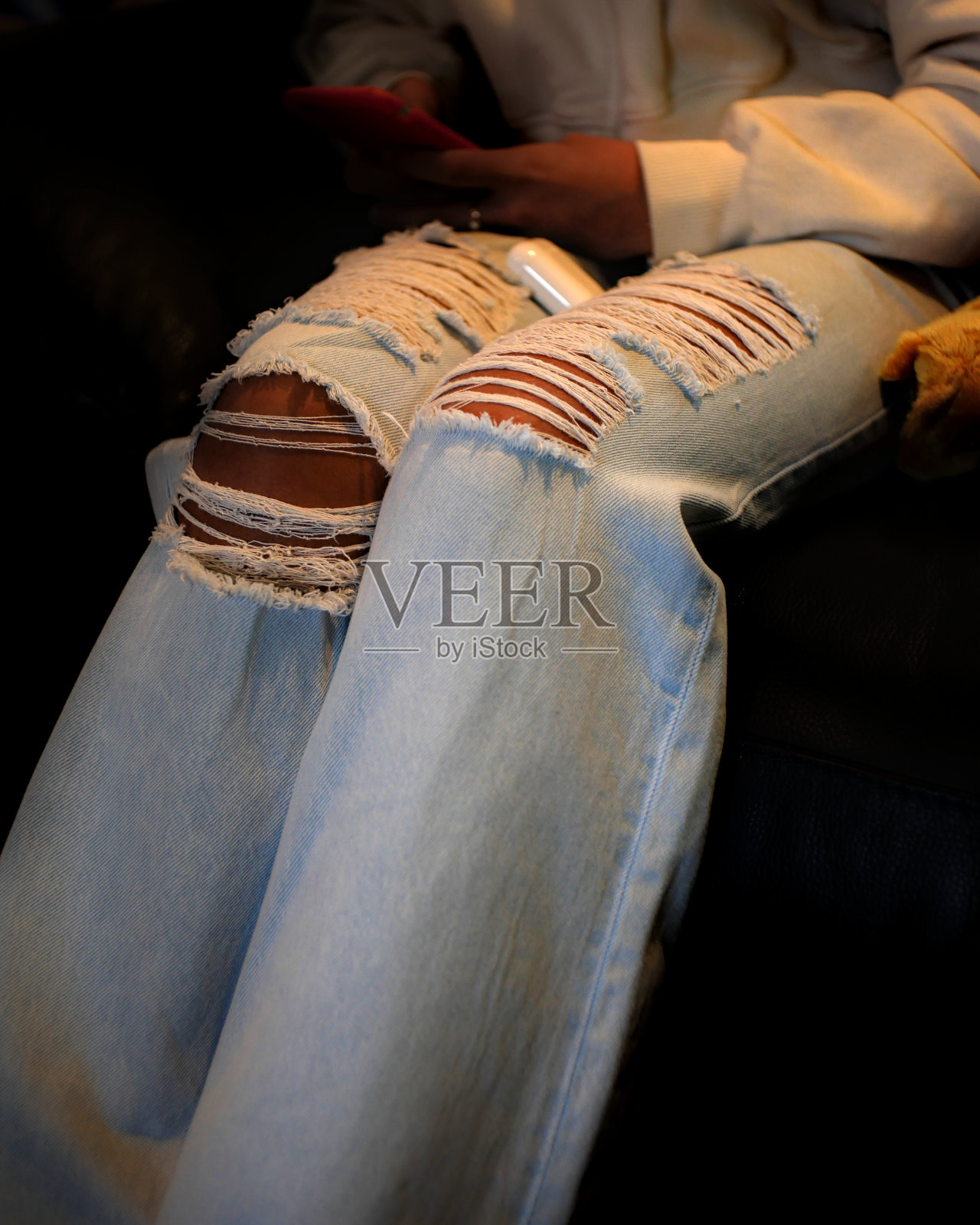 一个穿着破洞牛仔裤的年轻女子的膝盖特写。照片摄影图片