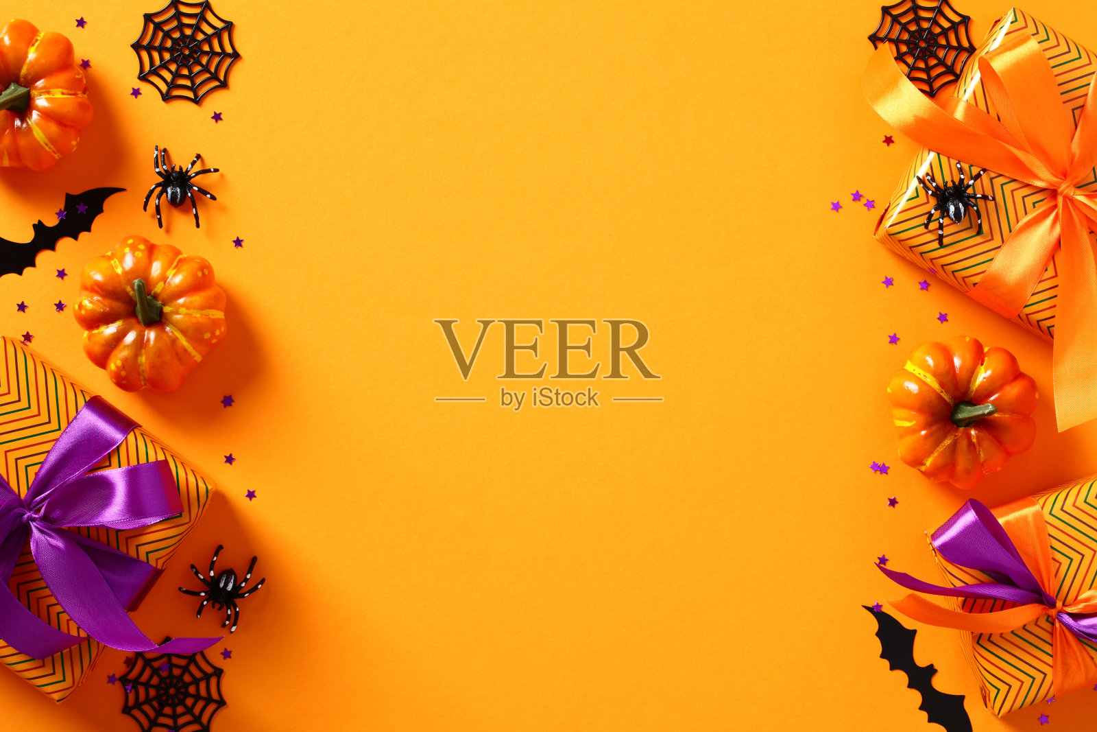 万圣节快乐节日贺卡模板。框架制成的万圣节装饰品，南瓜，礼物，蜘蛛，网，蝙蝠在橙色的桌子上。平铺，俯视图，复制空间。照片摄影图片