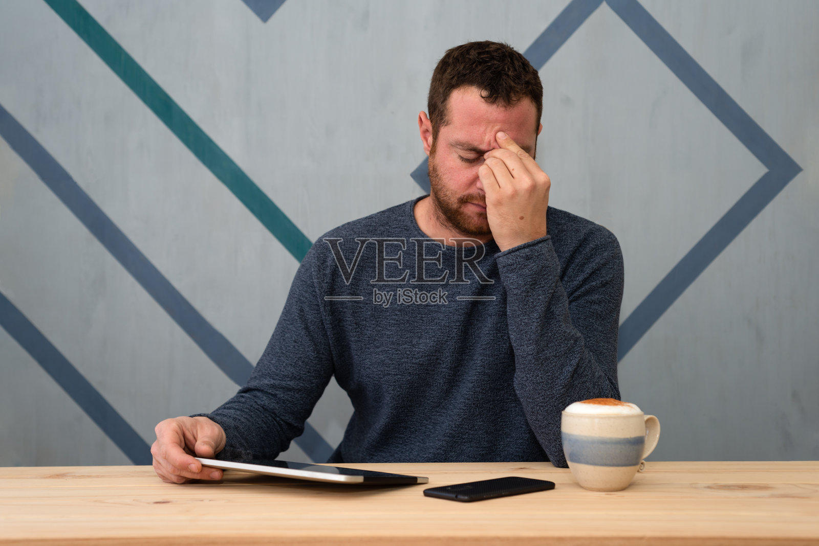 有胡子的年轻男子坐在他的工作场所，感到压力和疲劳。照片摄影图片