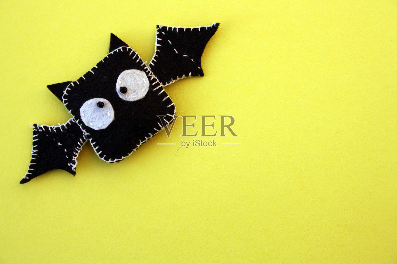 一只用毛毡在黄色背景上缝制的黑色蝙蝠。万圣节的玩具。照片摄影图片