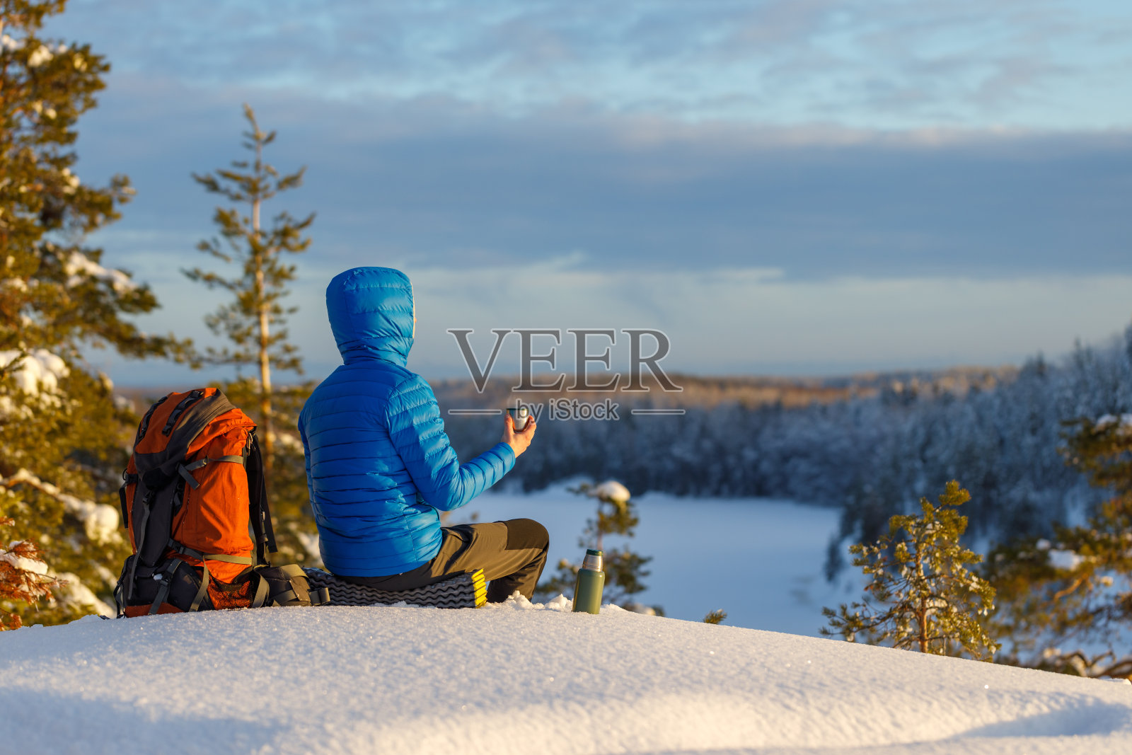晚上，一个背着背包的男人坐在冬天的森林里，喝着美味的茶。照片摄影图片