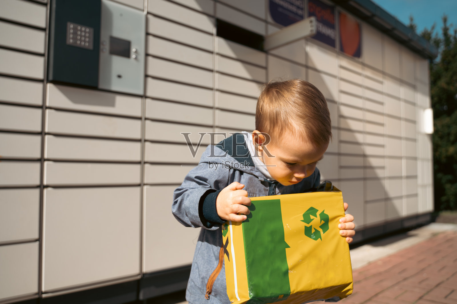 小包裹。孩子们在自动投寄终端机旁的快递箱旁张望。自助式邮政终端机及包裹递送概念。照片摄影图片