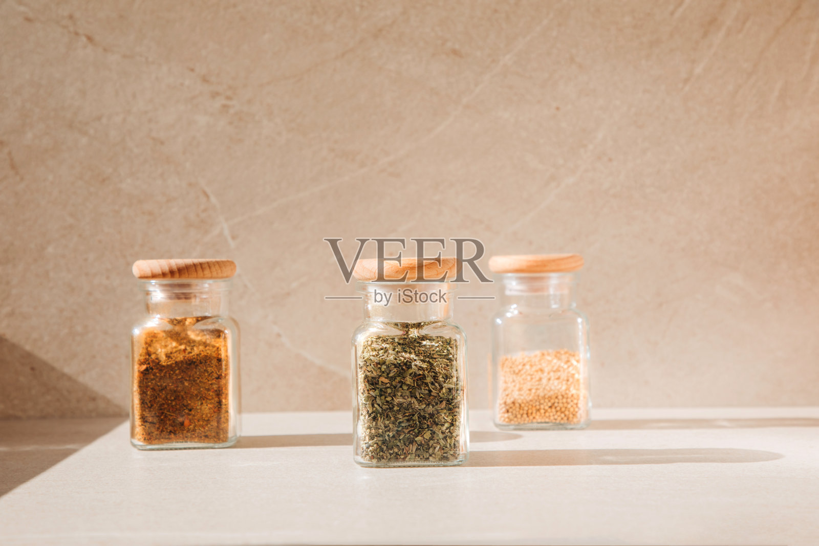 香料在玻璃罐中，浅色的石头背景与阴影。辣椒粉、香草、芥末照片摄影图片