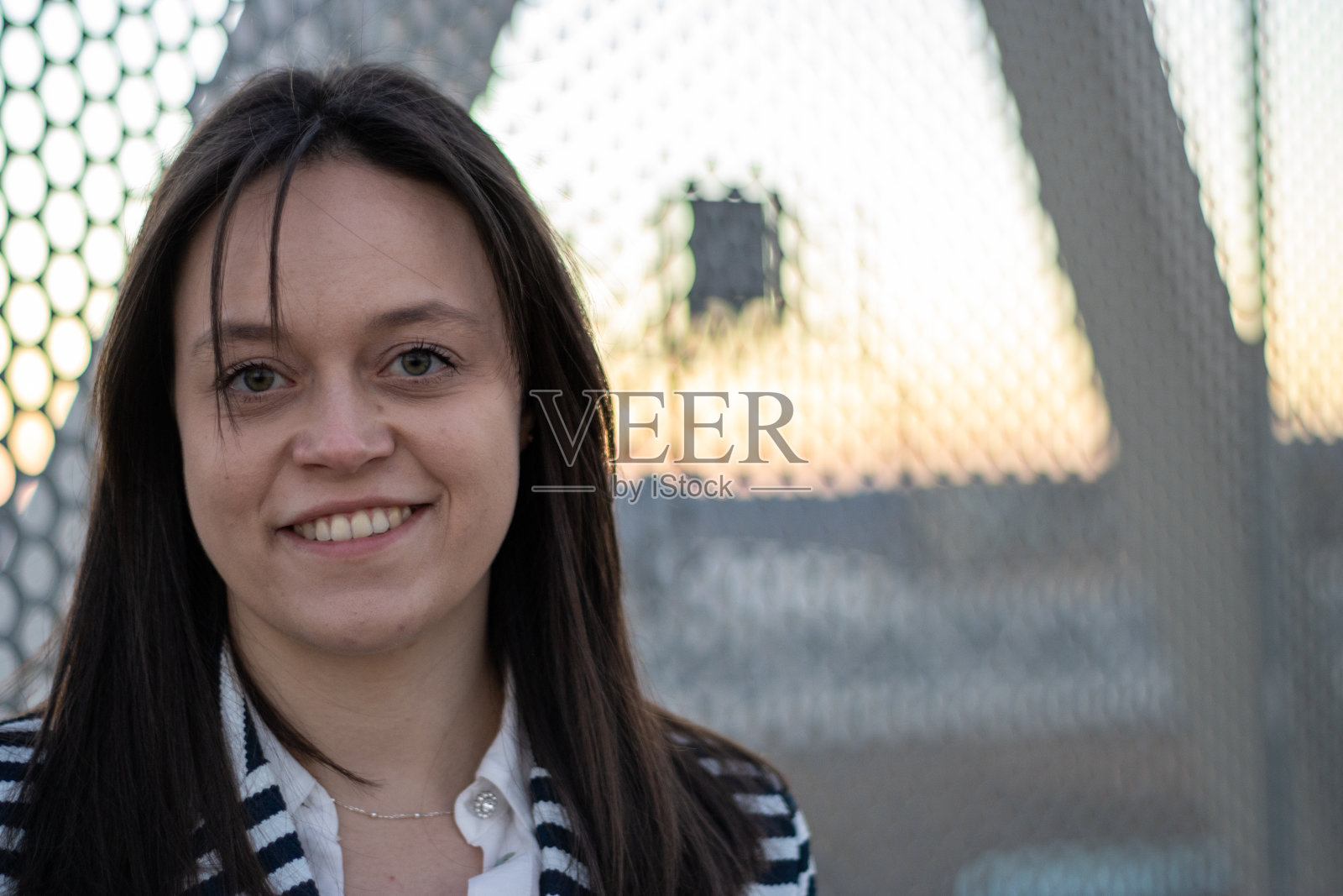 画像的年轻女子微笑和看着相机对着一个链环围栏户外照片摄影图片