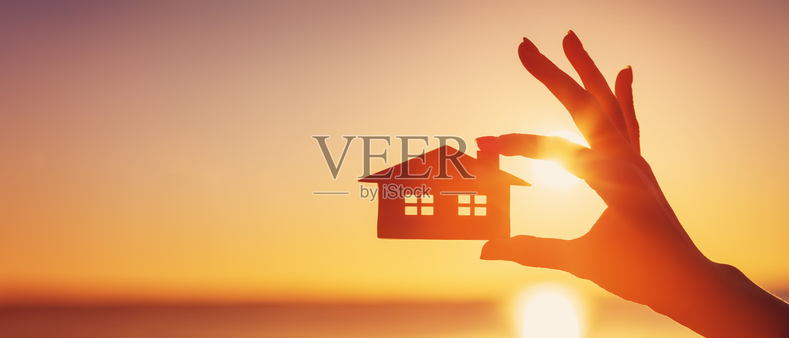 夕阳西下，女子手握房屋模型照片摄影图片