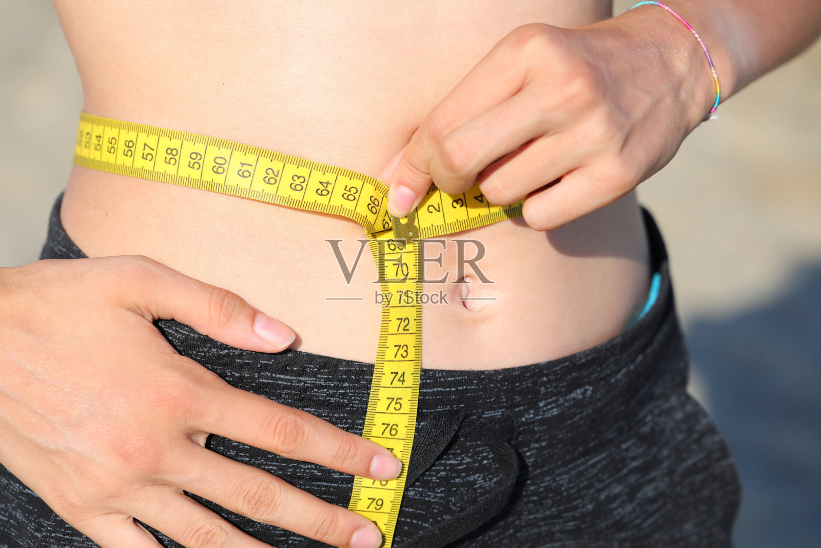 苗条的年轻女模特用卷尺测量自己的腰围，单位是厘米照片摄影图片