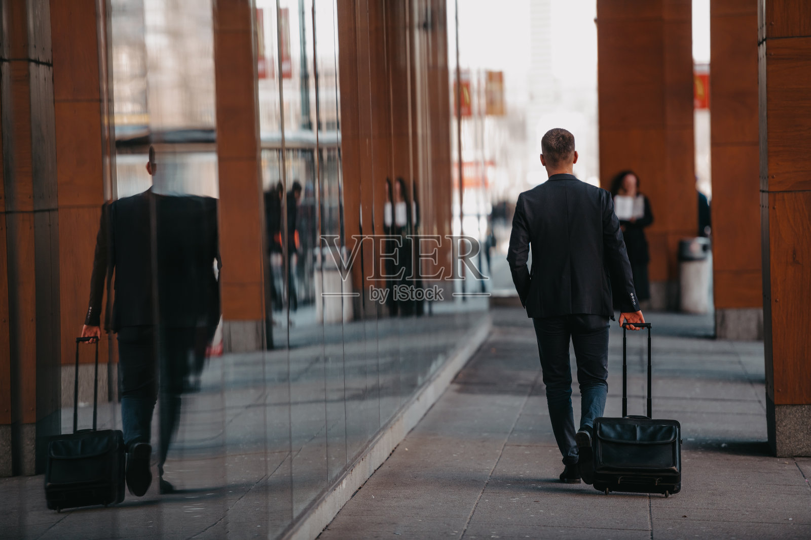 去机场候机楼。自信的商人旅行者走在城市的街道上，拉着他的行李箱，喝着咖啡，用智能手机说话照片摄影图片