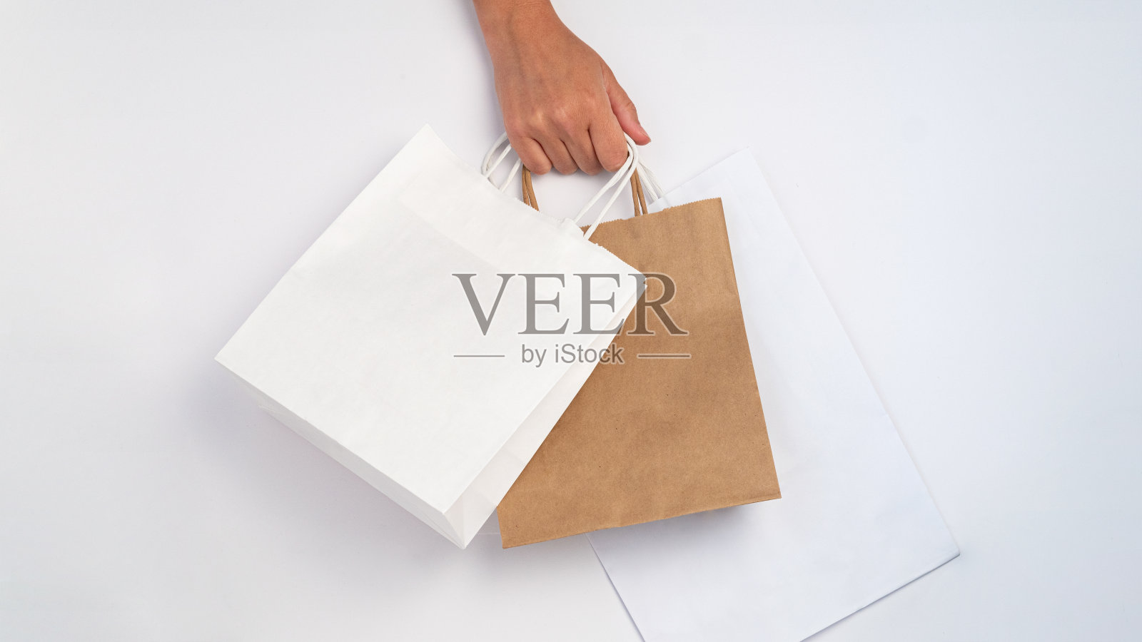 女人手拎购物袋，白色和牛皮纸款式，打折出售照片摄影图片