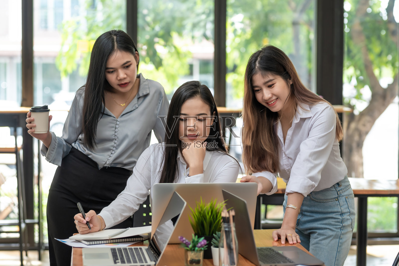 一群年轻的亚洲女商人快乐成功的工作会议头脑风暴使用笔记本电脑，文件被放在办公桌上。照片摄影图片