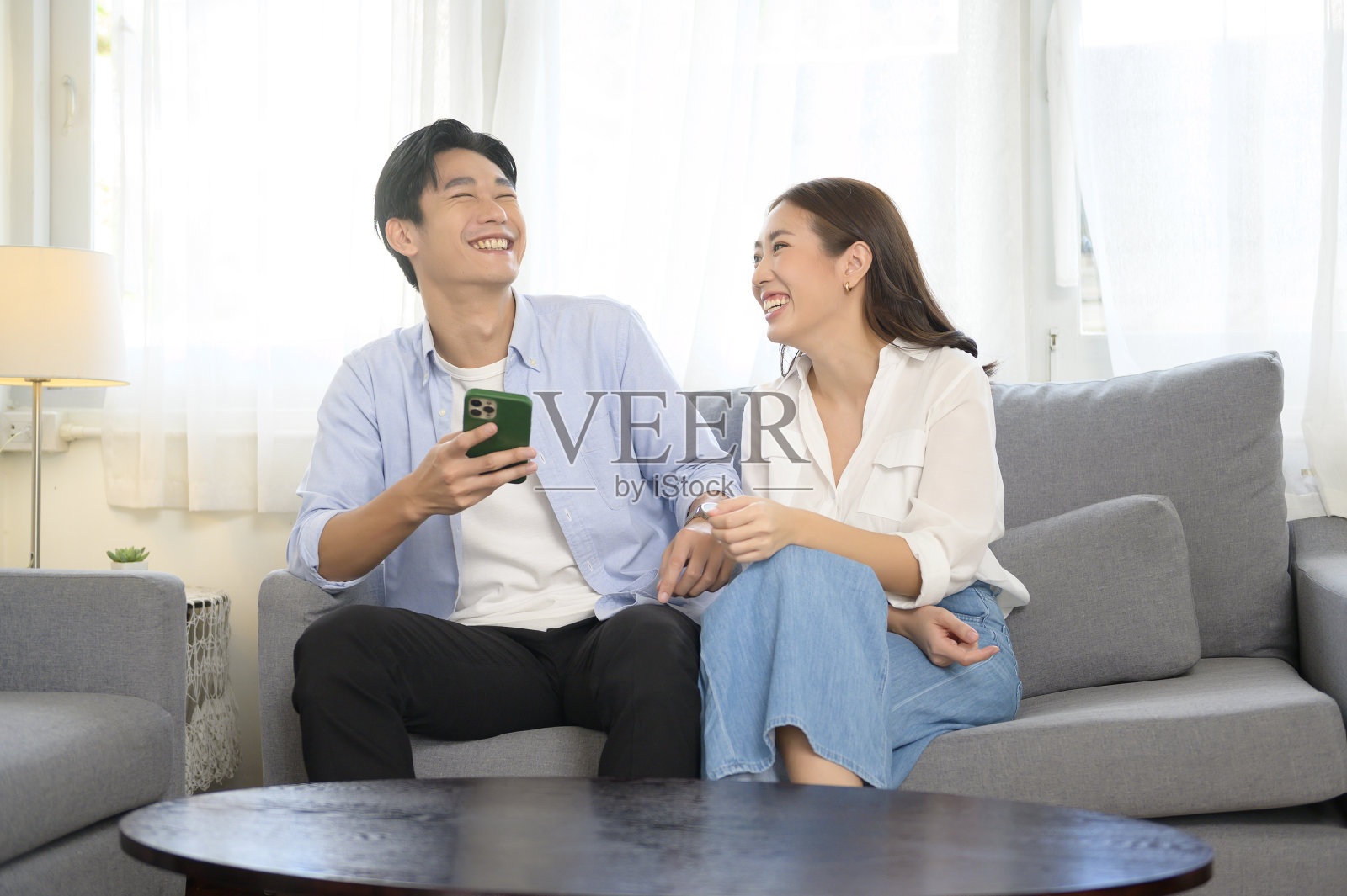 年轻的亚洲夫妇微笑着在家里的客厅使用智能手机照片摄影图片