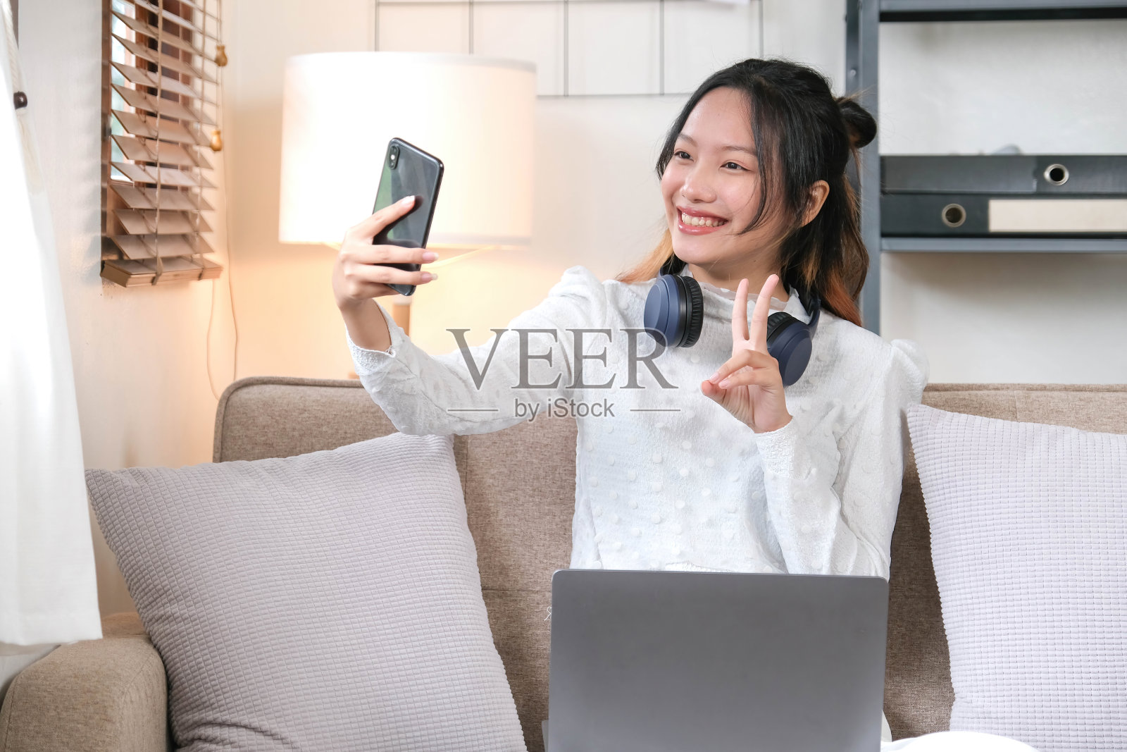 一位快乐、开朗的年轻亚洲女性在客厅放松，享受着通过智能手机与朋友视频通话的乐趣。照片摄影图片