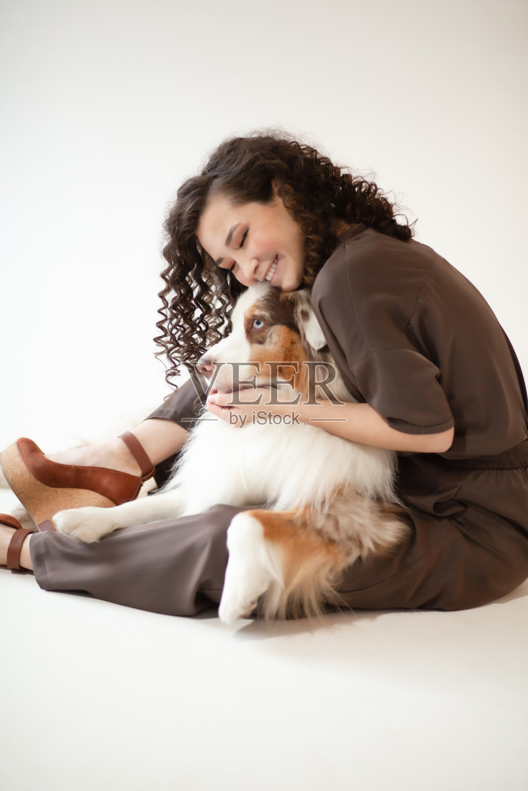 快乐的年轻女子抱着澳大利亚牧羊犬坐在地板上照片摄影图片