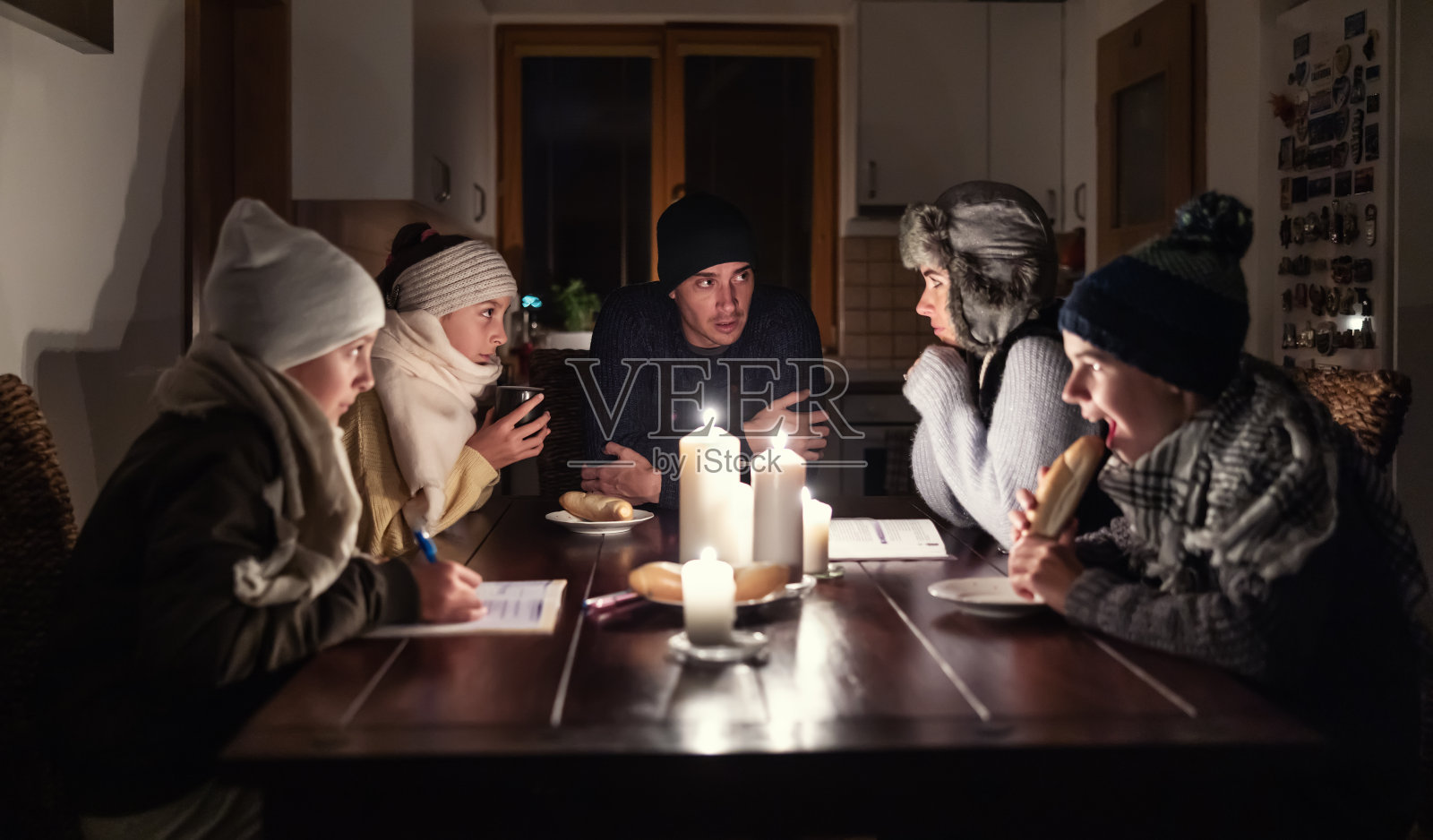 孩子们在蜡烛的灯光下吃饭、学习，家长们则在餐桌上讨论着因能源危机而没有光和热的压力。照片摄影图片