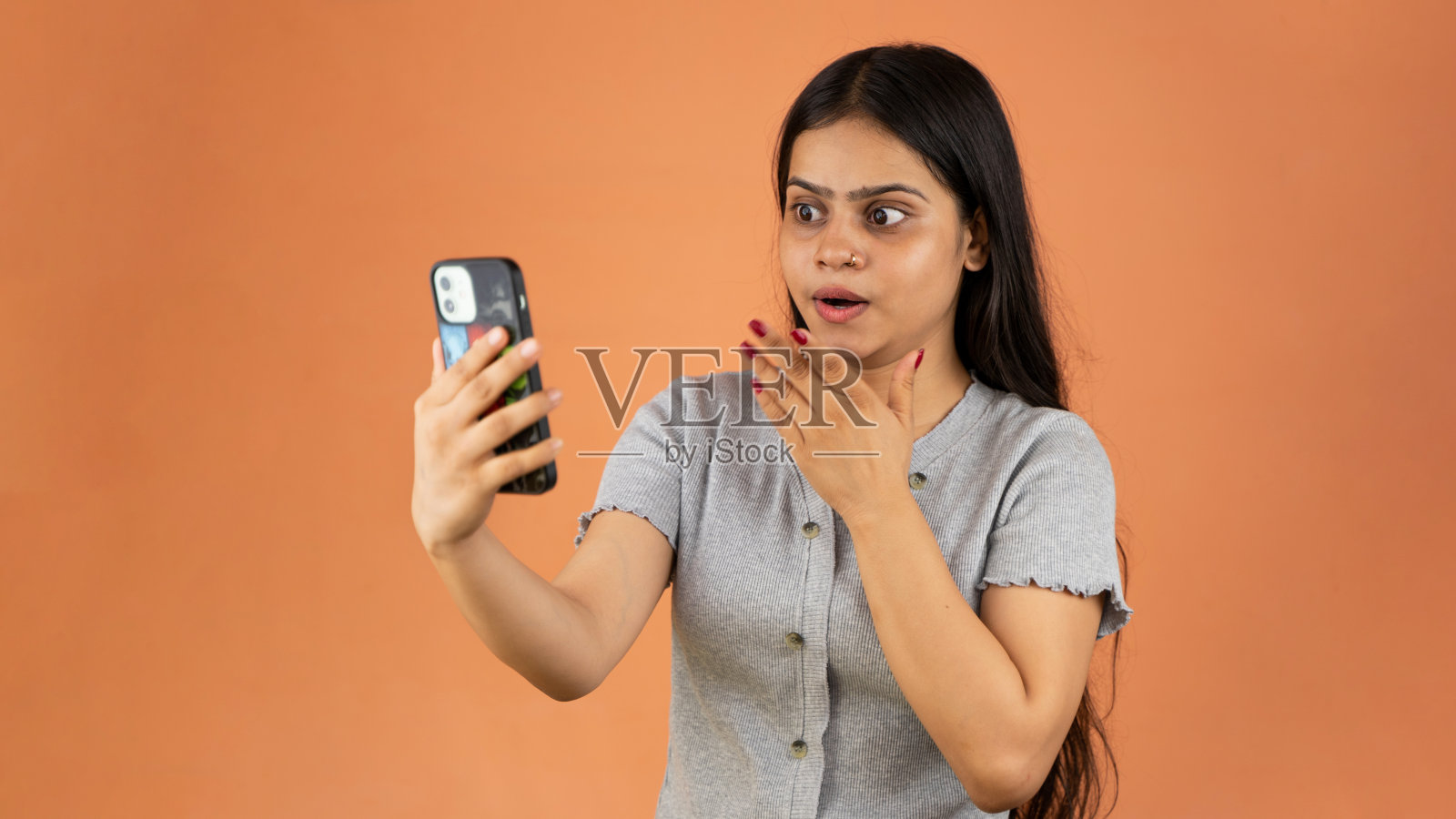 惊讶的年轻女子用手机，震惊的印度女子拿着智能手机，看着手机屏幕，隔离在彩色背景上照片摄影图片
