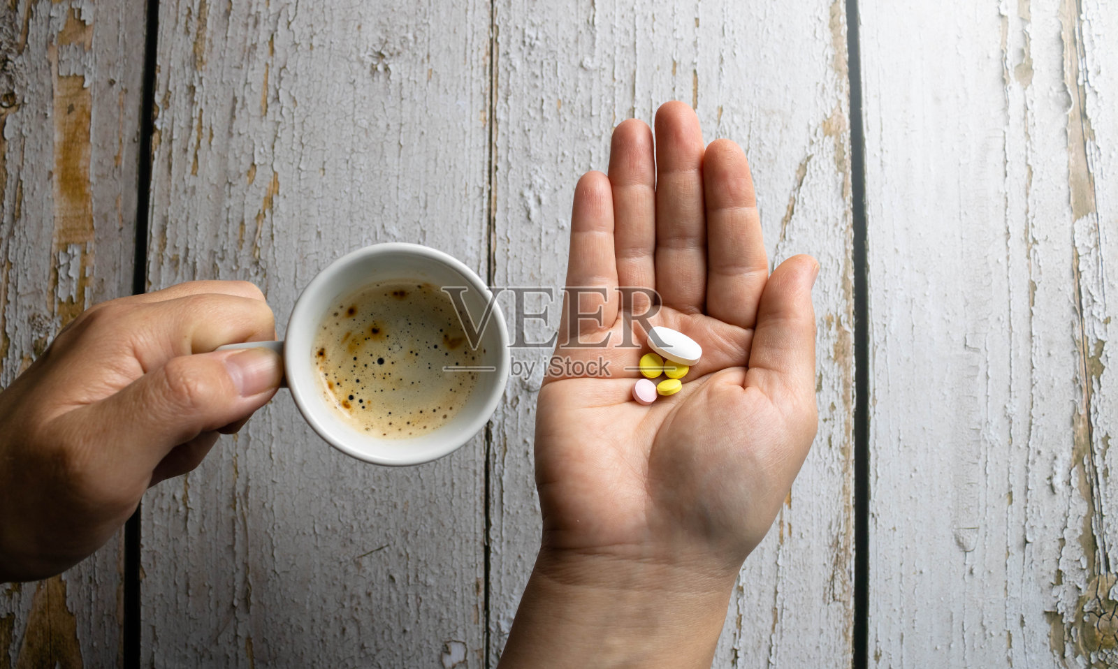 一个白人妇女的两只手，左手拿着药物和维生素的混合物，右手拿着杯子里的咖啡。指食物、药物和健康选择。照片摄影图片