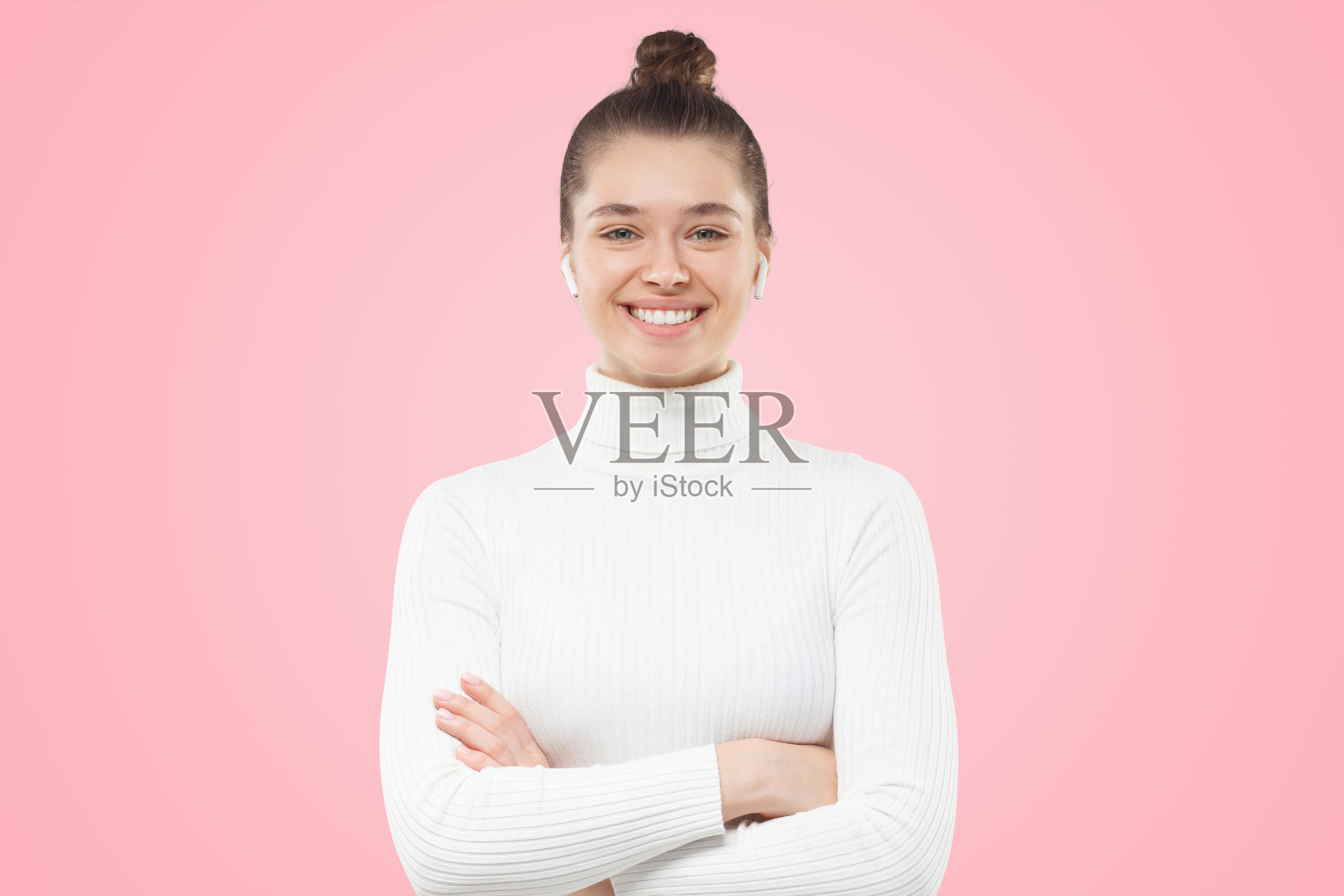 女孩盘发，双臂交叉，穿着白色毛衣，自信的微笑看着观众照片摄影图片