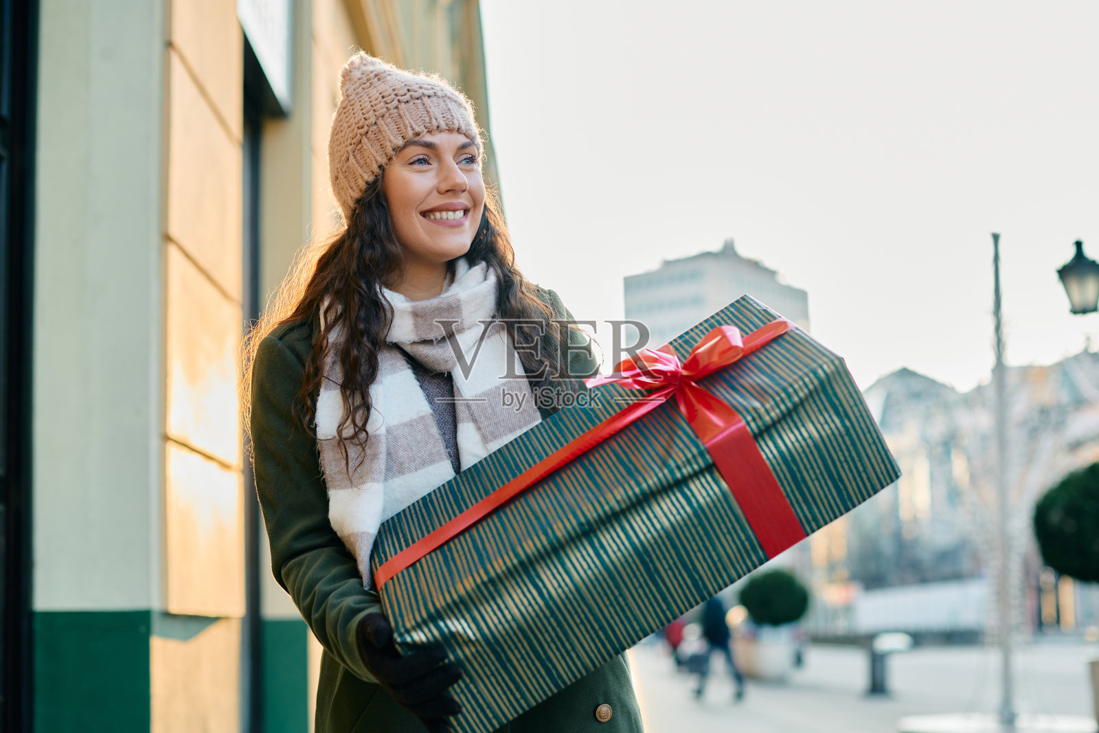 年轻的微笑的妇女带着包装好的礼物走在城市在寒假。照片摄影图片