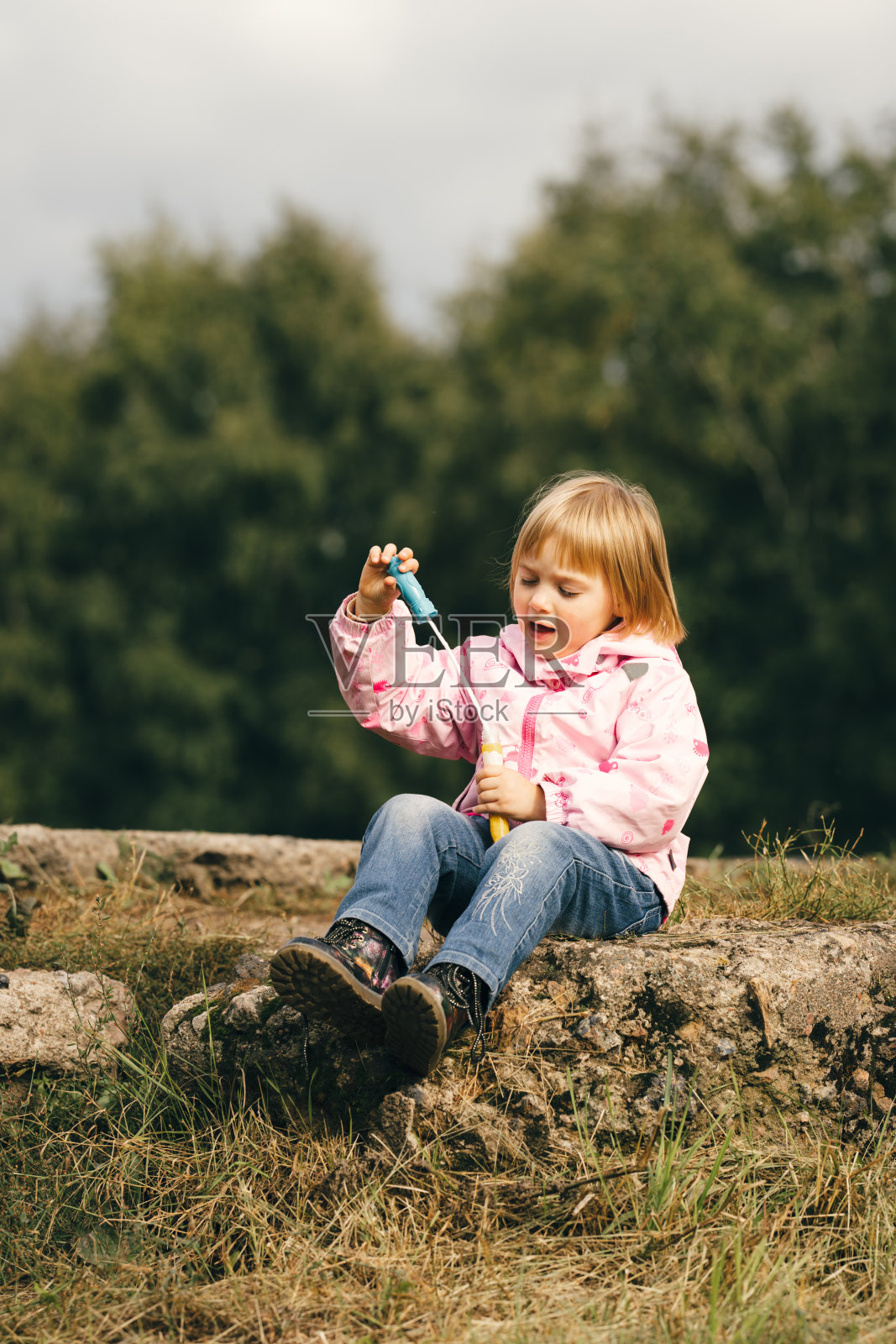 穿着粉色外套的学龄前小女孩在户外玩肥皂泡。照片摄影图片