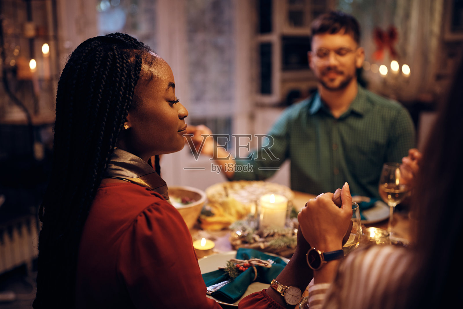 一名黑人妇女在感恩节晚餐前和她的朋友们手牵手祈祷。照片摄影图片