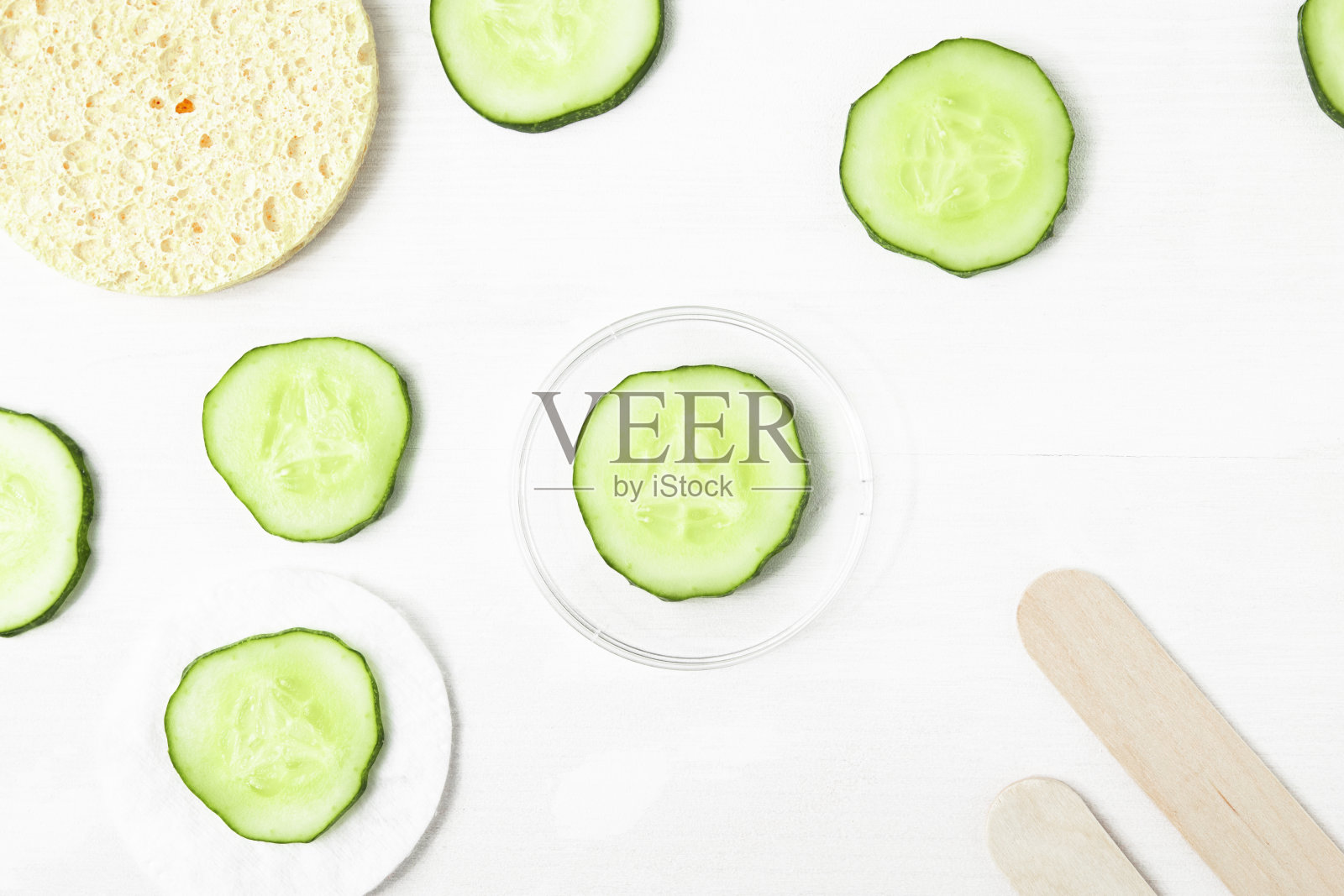 白色背景上的新鲜的绿色黄瓜片和配件，海绵和铲子自制的保湿面膜俯视图。照片摄影图片