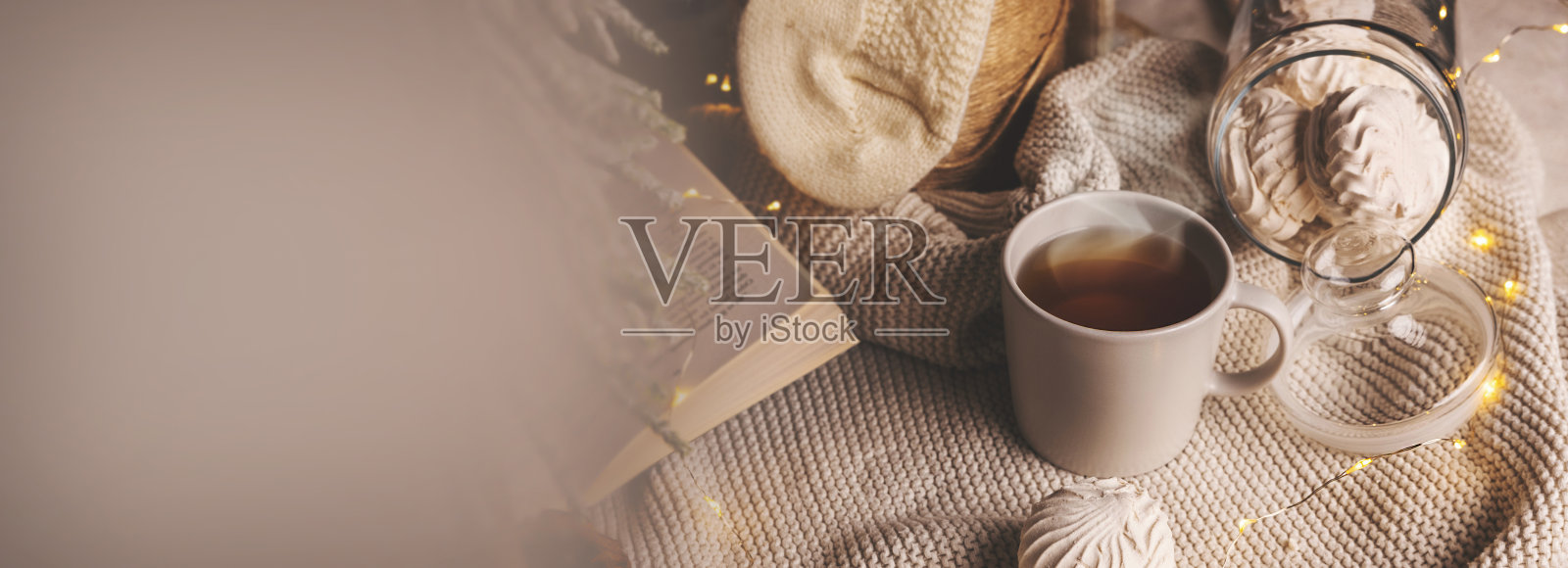 舒适的冬天组成一杯茶，糖果和圣诞灯在针织毯子。带有复制空间的横幅照片摄影图片