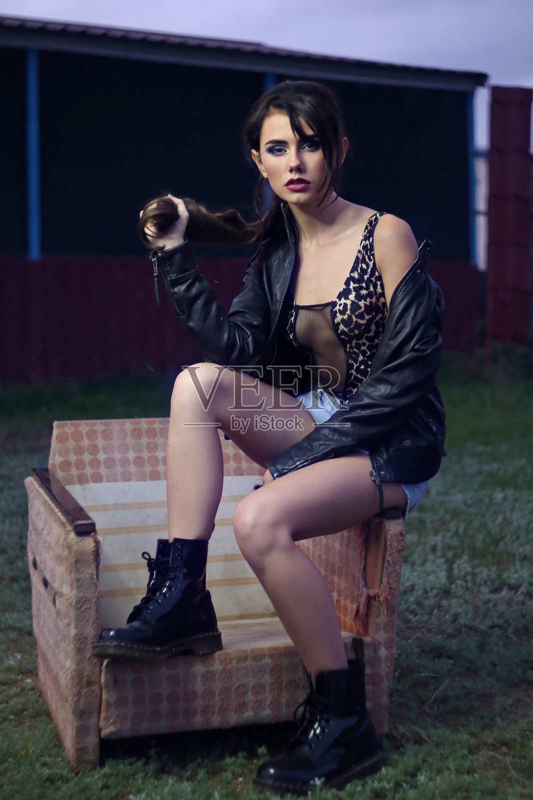 漂亮时髦的女孩坐在旧扶手椅上，穿着短裤，靴子和夹克照片摄影图片