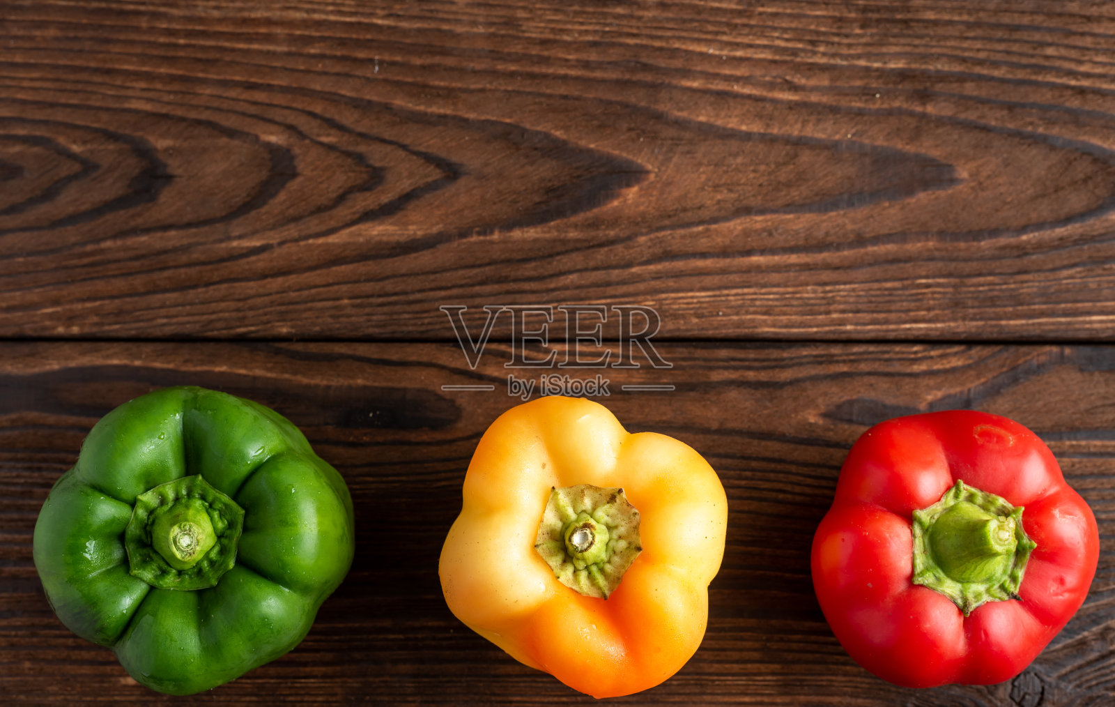 三种不同颜色的辣椒放在木制背景上照片摄影图片