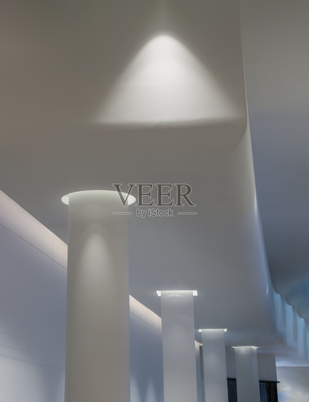 混凝土室内空间，白色的圆形柱子排列着长长的线条，灯光投射在墙壁和柱子上。照片摄影图片