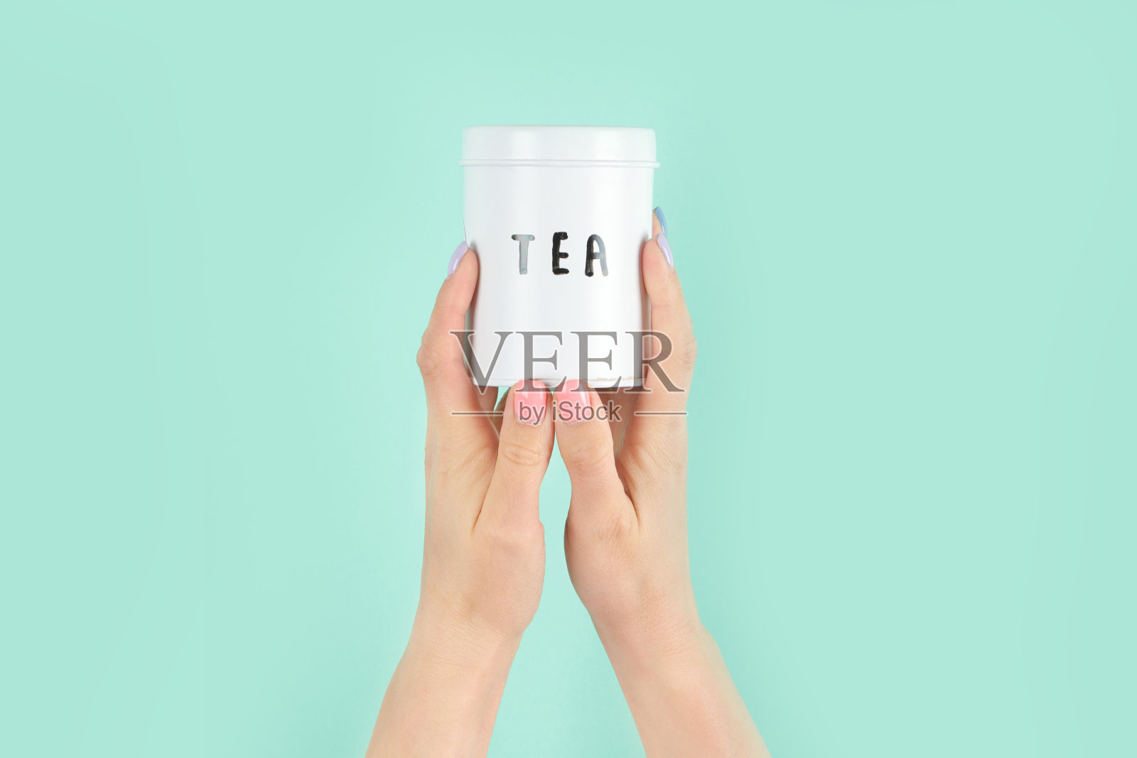 手臂举起，捧着绿色背景的茶杯。照片摄影图片