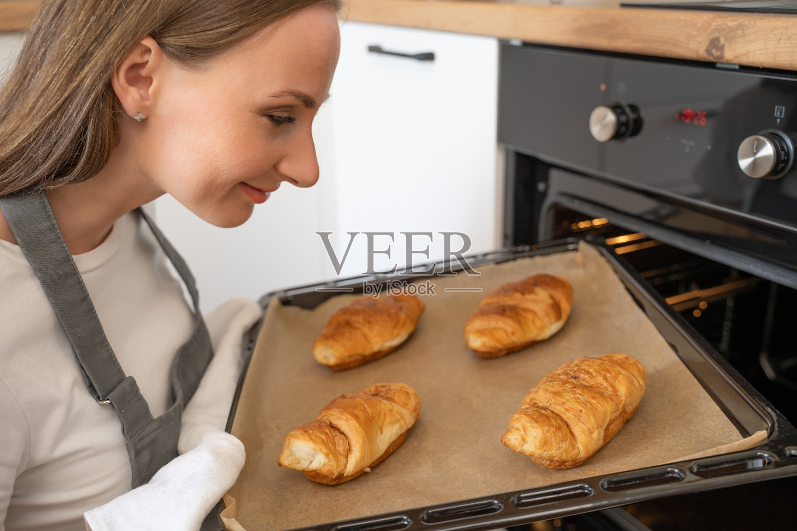 年轻女子从厨房拿出一盘烤羊角面包照片摄影图片