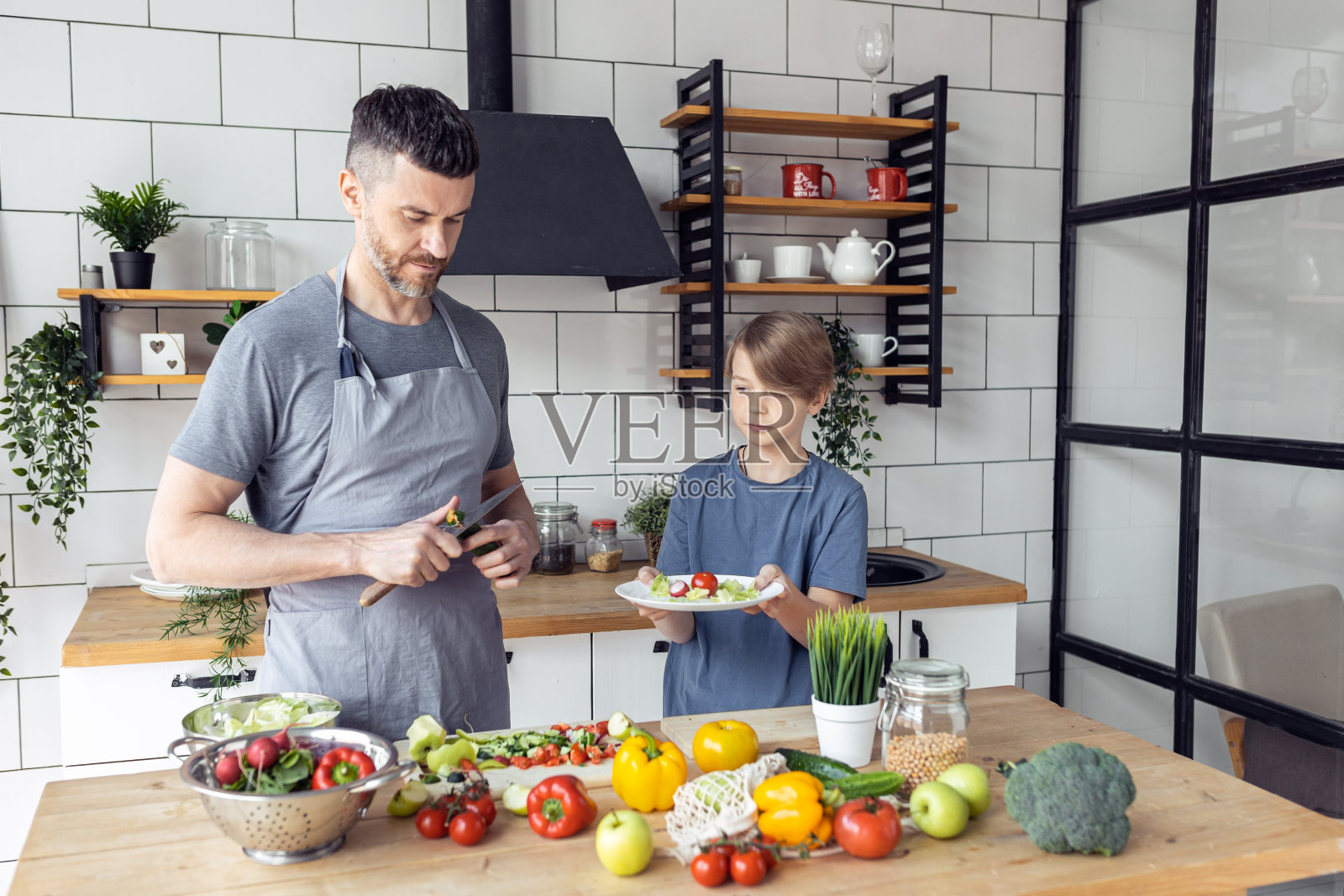 英俊的父亲和他十几岁的儿子一起度过美好时光。男人做家务，做健康的蔬菜沙拉，在家里的厨房里做美味的食物照片摄影图片