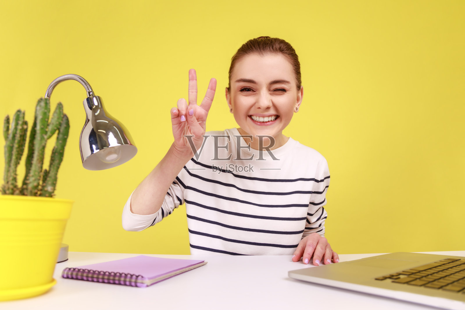 坐在工作场所的妇女，看着相机的视角，照片的视角，展示着胜利的姿态。照片摄影图片