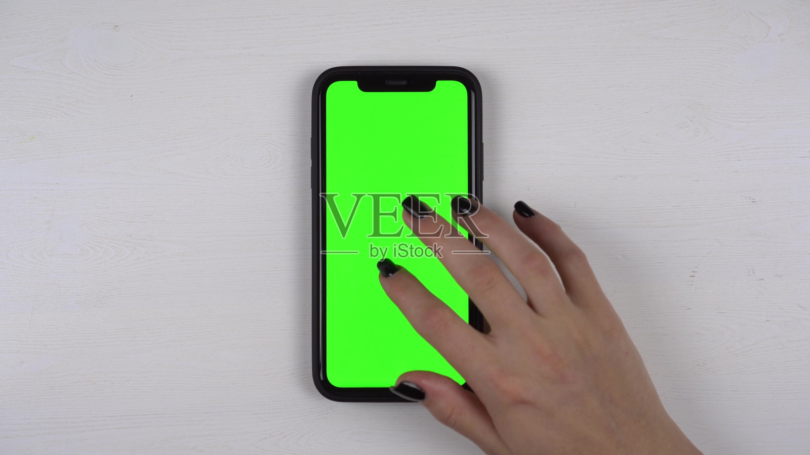 一位女士躺在桌子上使用智能手机。手机屏幕是绿色的。女孩用手指轻敲显示器。手关闭。照片摄影图片