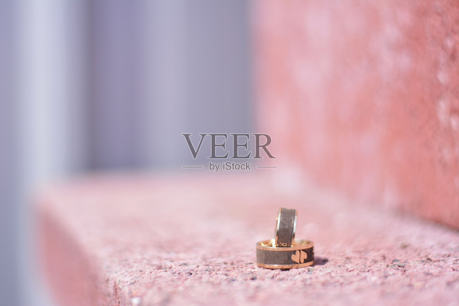 一对新婚夫妇的金色戒指在粉色模糊的背景上的特写-婚礼的概念照片摄影图片