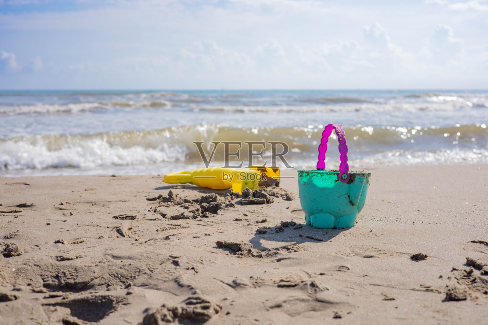 西班牙巴伦西亚的海滩，萨普拉亚港，在那里你可以看到一个绿色和紫色的塑料桶在沙滩上，一个黄色的抓手，和一些海浪在地中海照片摄影图片