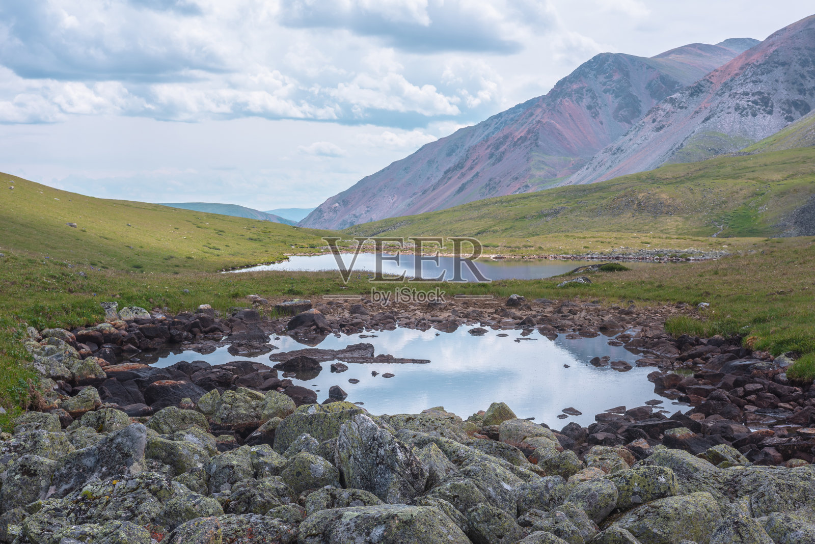 风景优美，多云的天空下，山谷中有两个山湖，绿色的山丘上有阳光。云影映在地衣石间的小湖水镜中，景色壮观。照片摄影图片