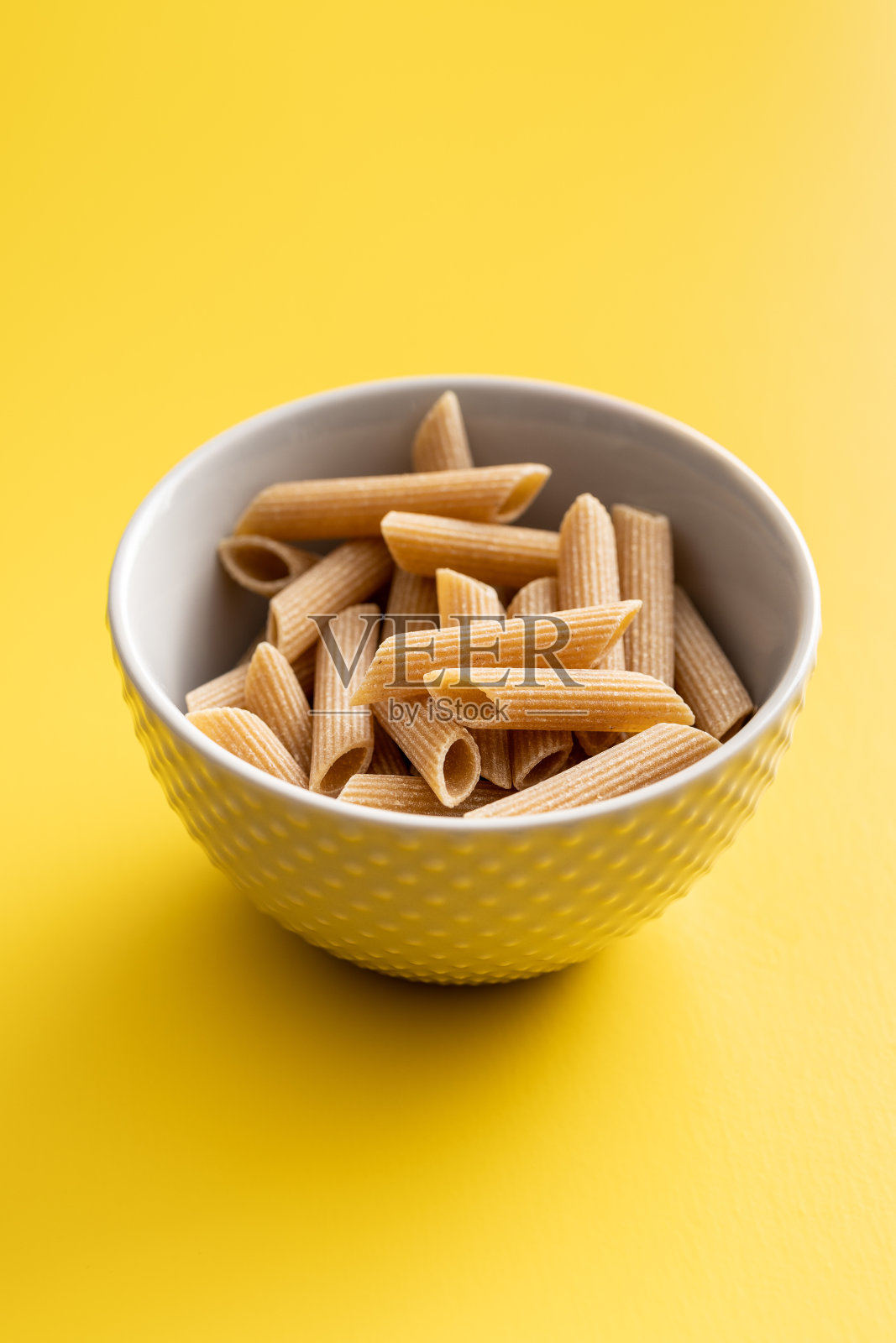 生的全谷物意大利面。在黄色背景的碗里生通心粉。照片摄影图片