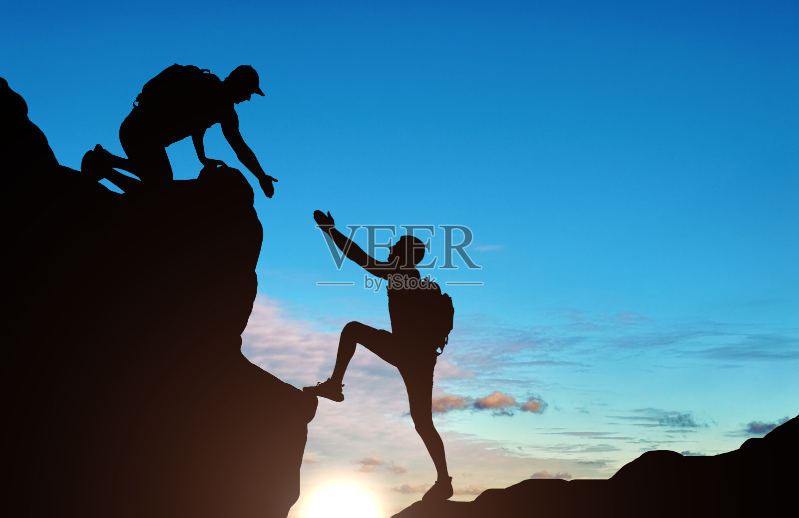 一个男性登山者向他的伙伴伸出援手的剪影照片摄影图片