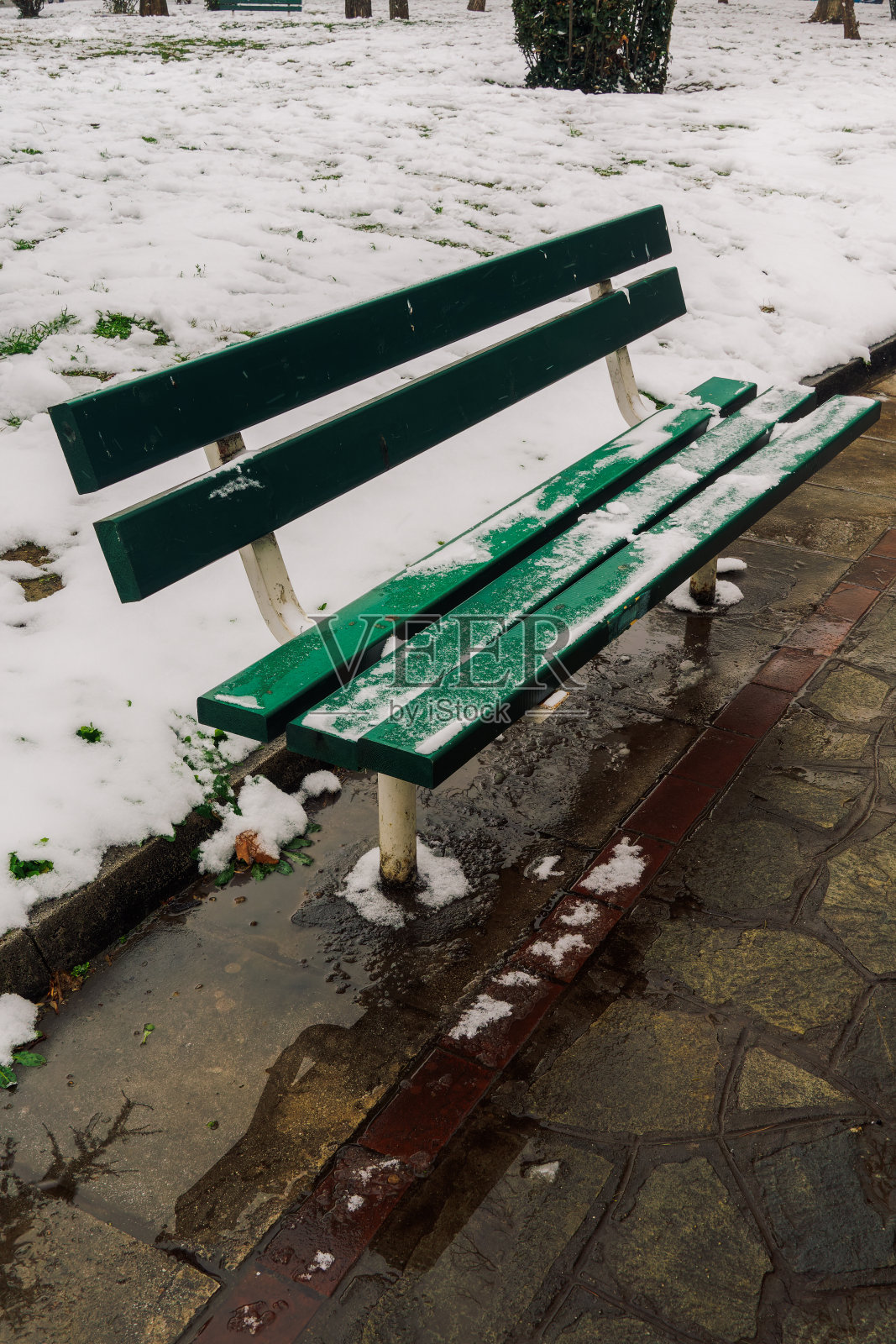 公园里的一张空空如也的绿木凳，部分被雪覆盖。照片摄影图片