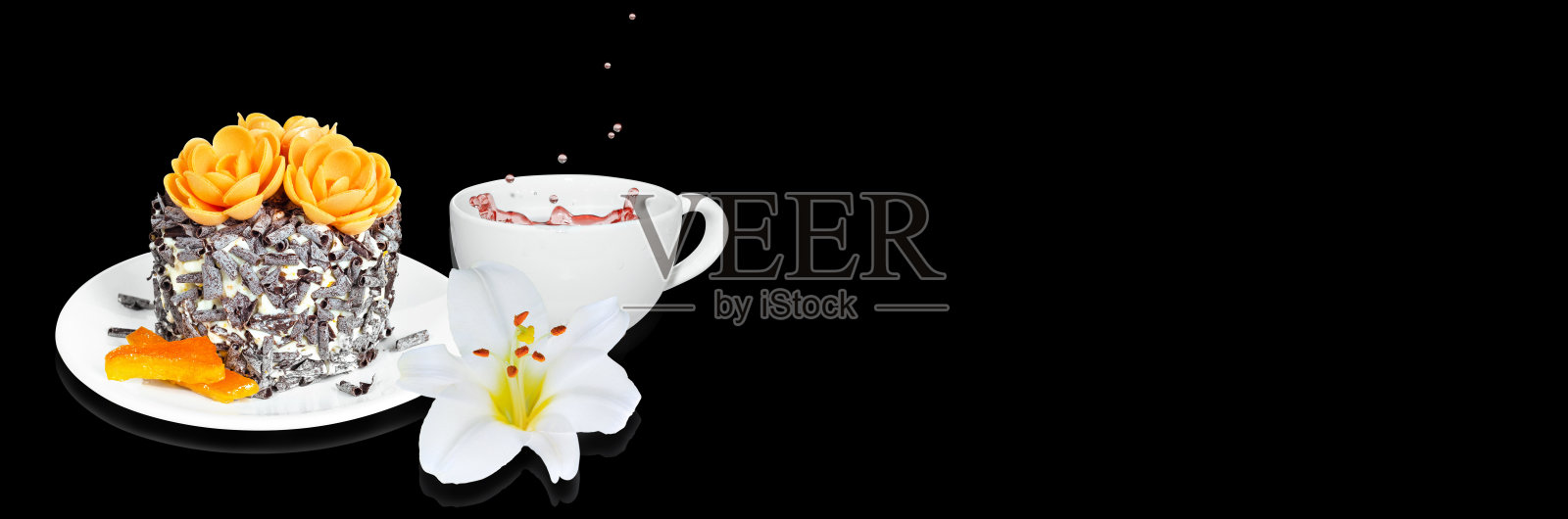 一个小蛋糕，配上蜜饯橙片和巧克力片，一杯茶和一朵花，背景是黑色宽屏。有选择性的重点,横幅照片摄影图片