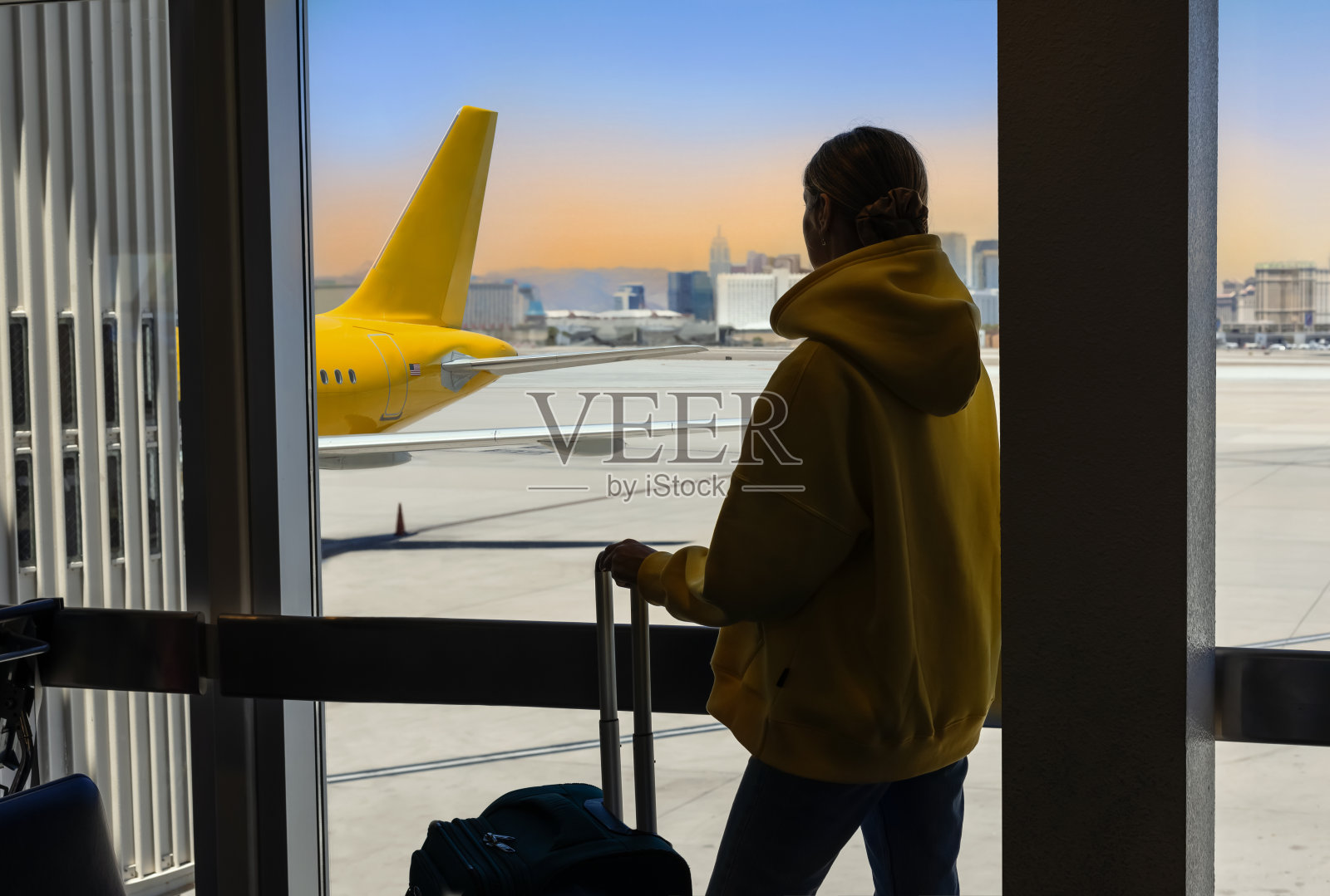 移民概念：年轻女子在机场，带着行李，悲伤地望着窗外的飞机照片摄影图片