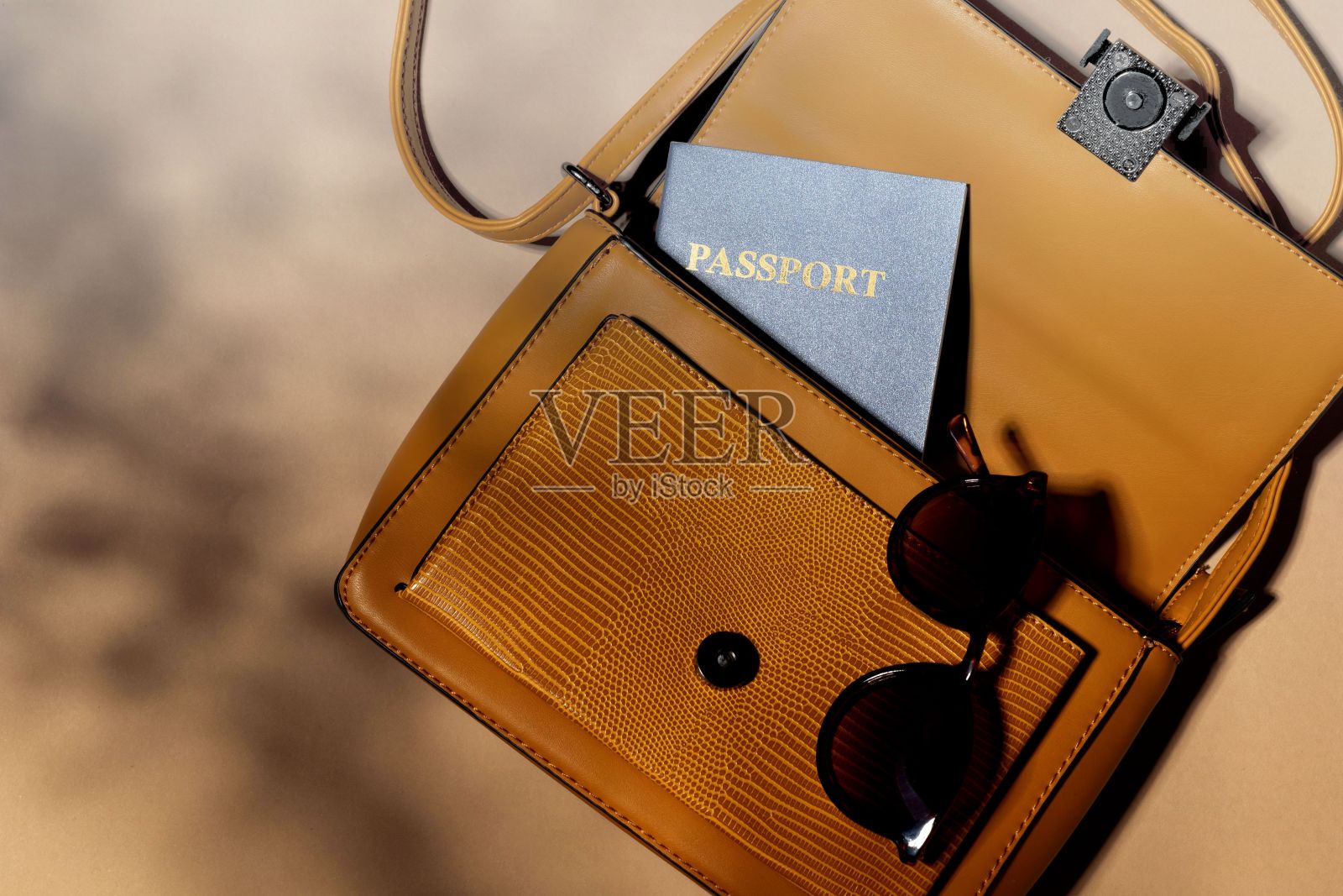 米色背景上的一个皮制手提包和一本护照和一副太阳镜的特写镜头照片摄影图片