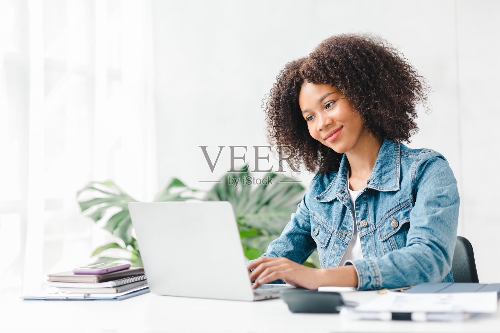 美国少女坐在白色的办公室里拿着笔记本电脑，她是一名学生在家里用笔记本电脑在线学习，大学生在线学习，在线网络教育的概念。照片摄影图片