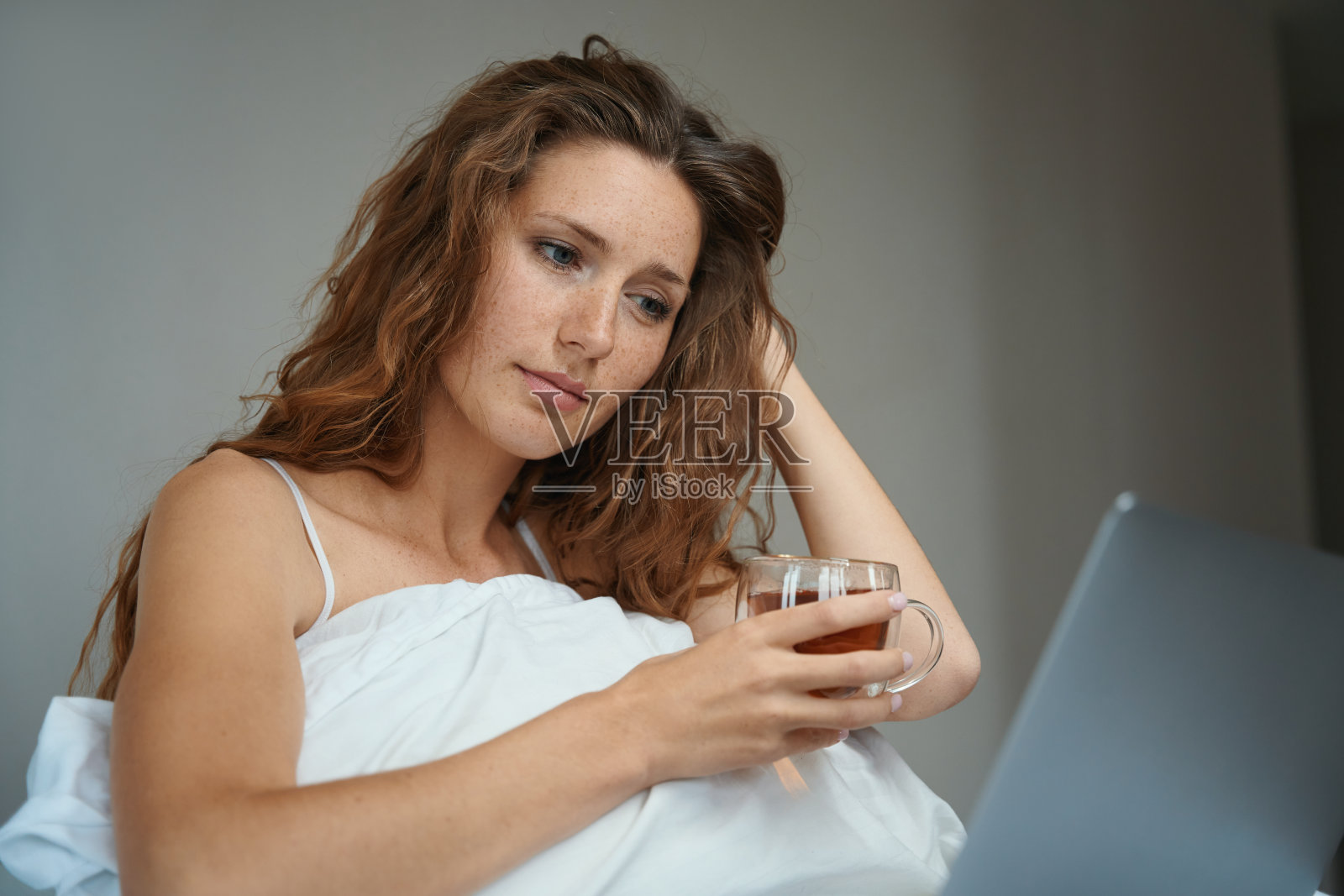 女人在床上端着一杯茶，用小玩意儿工作照片摄影图片