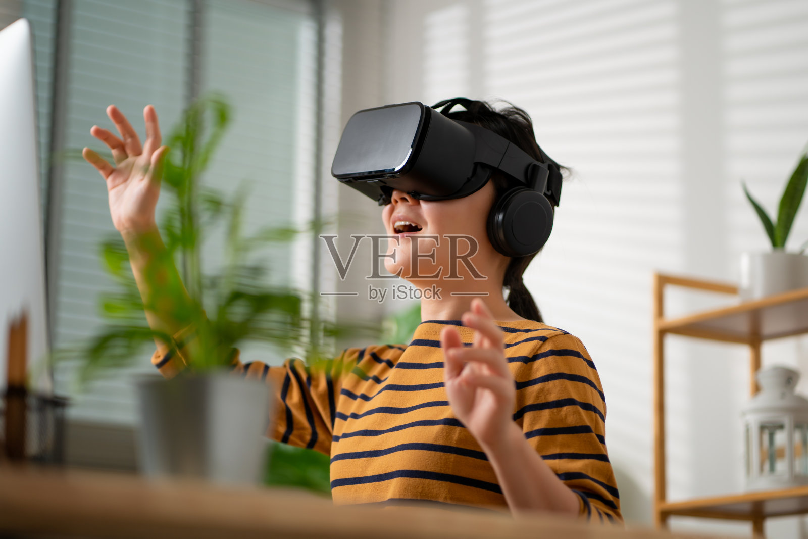 亚洲女性戴着VR头戴设备，在空中触摸，在家里办公室微笑。照片摄影图片