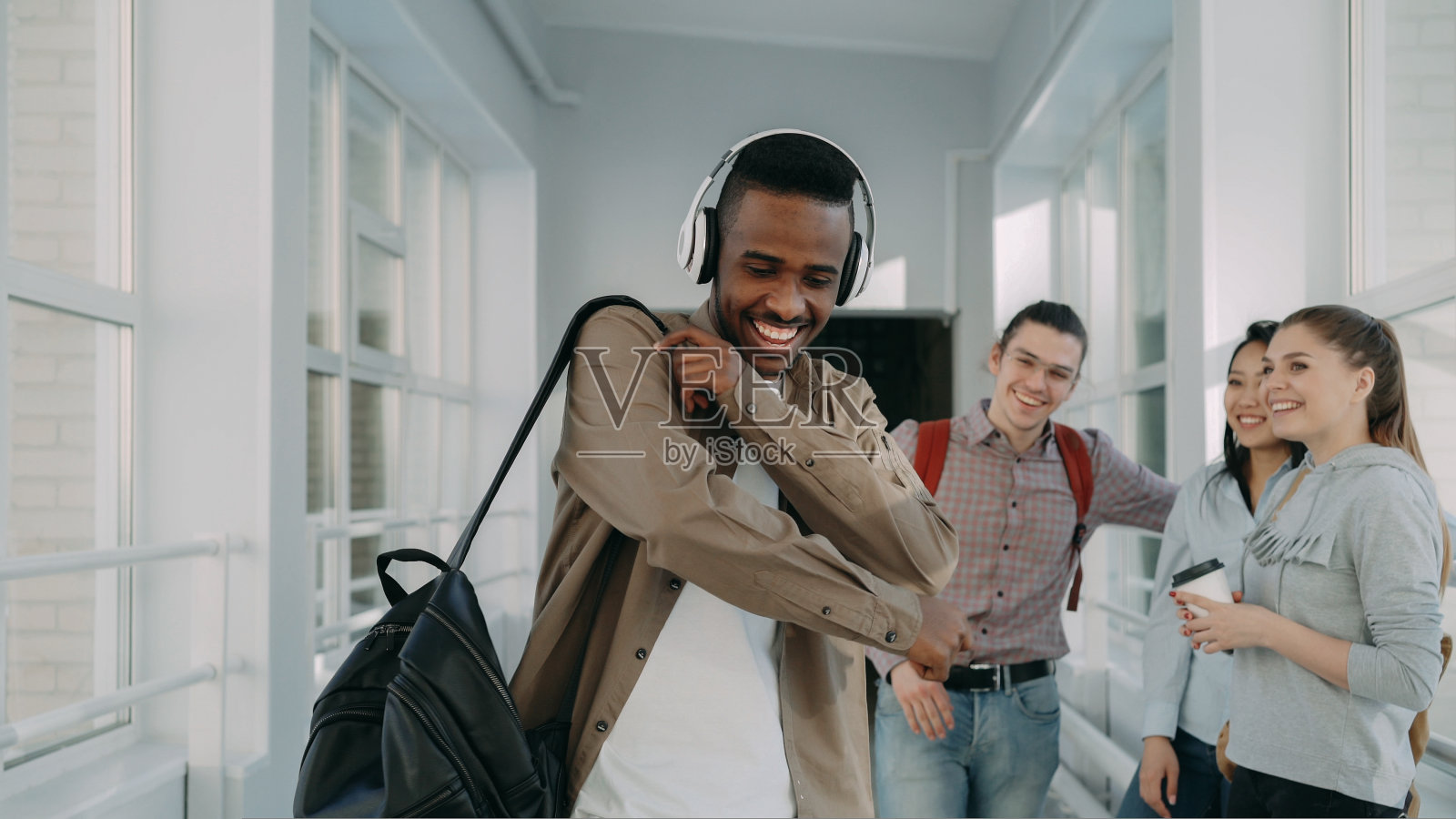 年轻英俊的非裔美国学生戴着大耳机，在大学的白色走廊里跳舞照片摄影图片