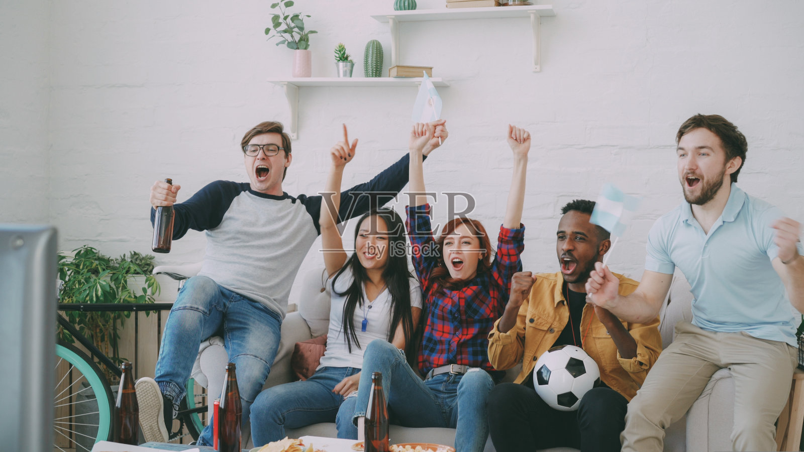 举着阿根廷国旗的朋友在家里一起看电视上的体育锦标赛，为最喜欢的球队获胜而高兴照片摄影图片