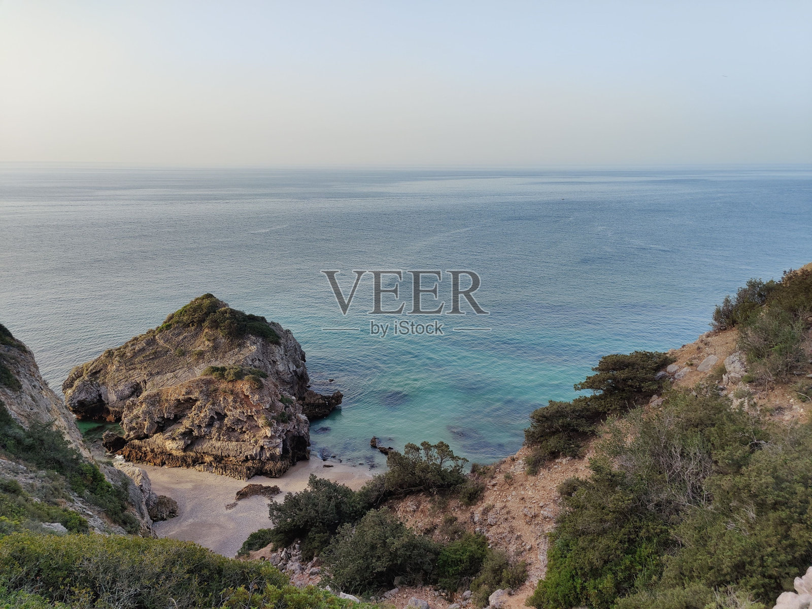 海滩上有灌木丛，一块大石头和大海，背景是晴朗的天空。照片摄影图片