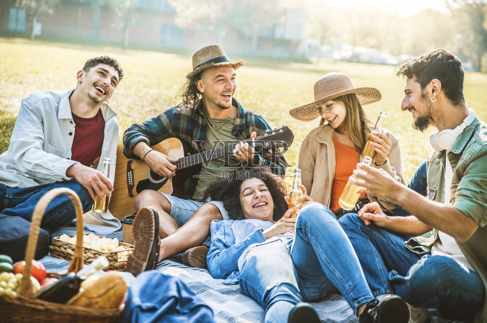 快乐的朋友在公园野餐-一群年轻人在一起唱歌弹吉他-年轻的生活方式和友谊理念照片摄影图片