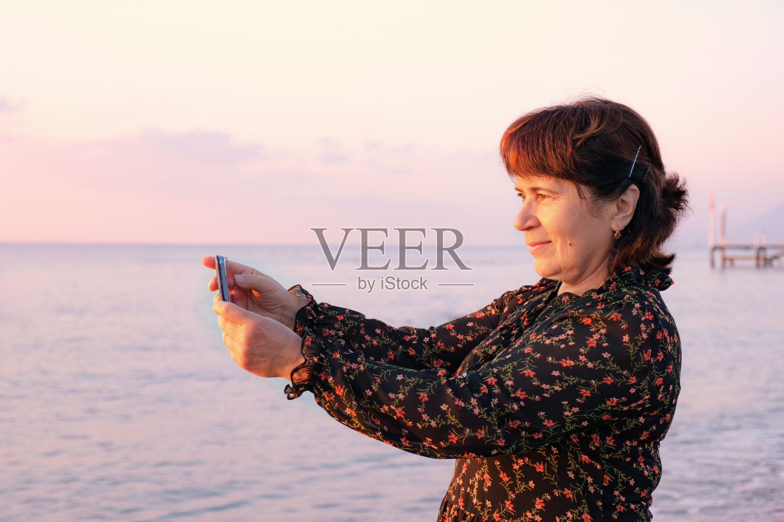 一位老年妇女在日出的阳光下拍摄海滩上的海景照片摄影图片